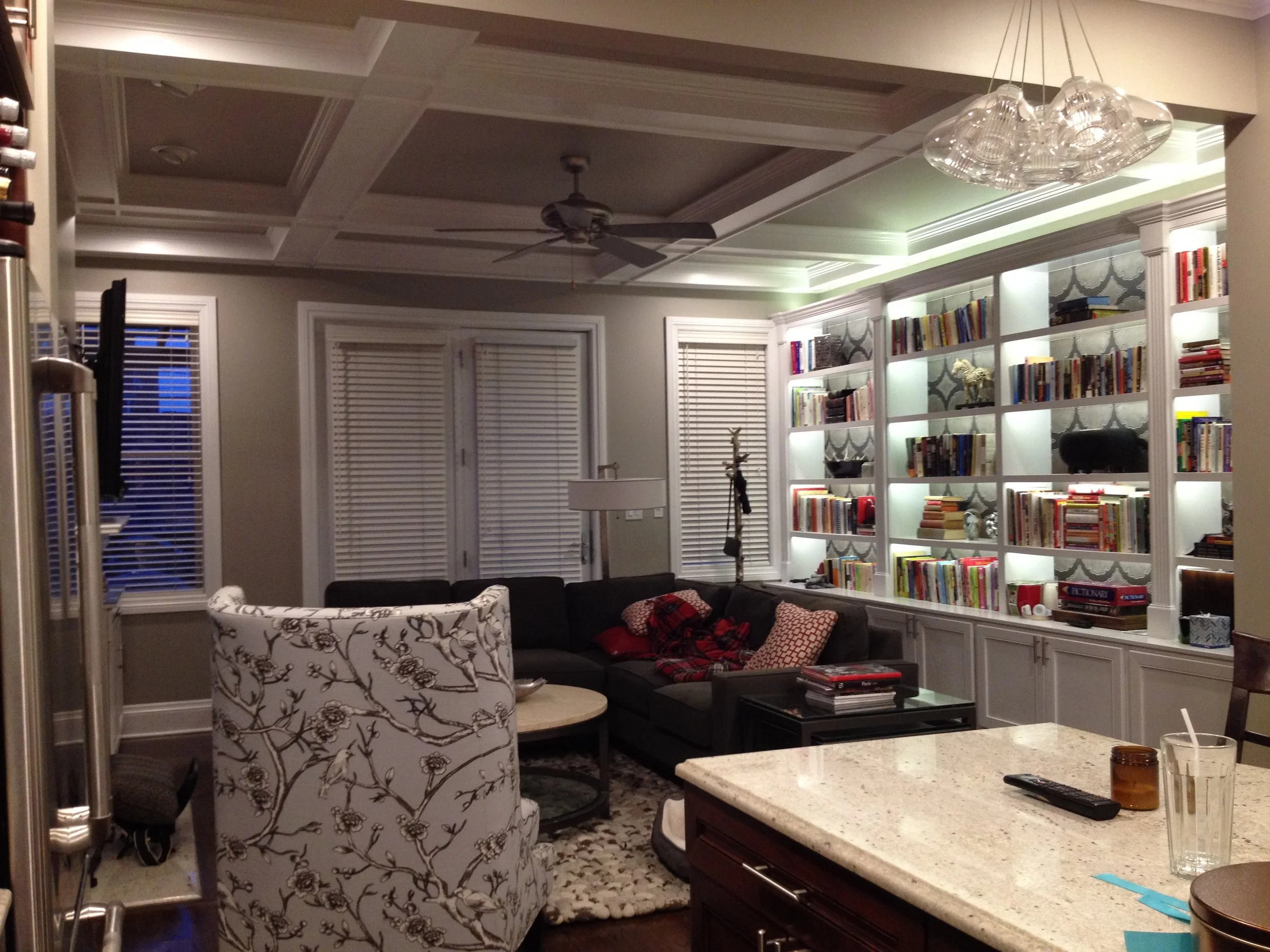  In this room all woodwork, ceiling, and walls were painted. The volume of white trim makes this family room feel crisp and clean.&nbsp;The neutral beige wall and ceiling color is accented with patterned wallpaper behind the bookshelves and patterned