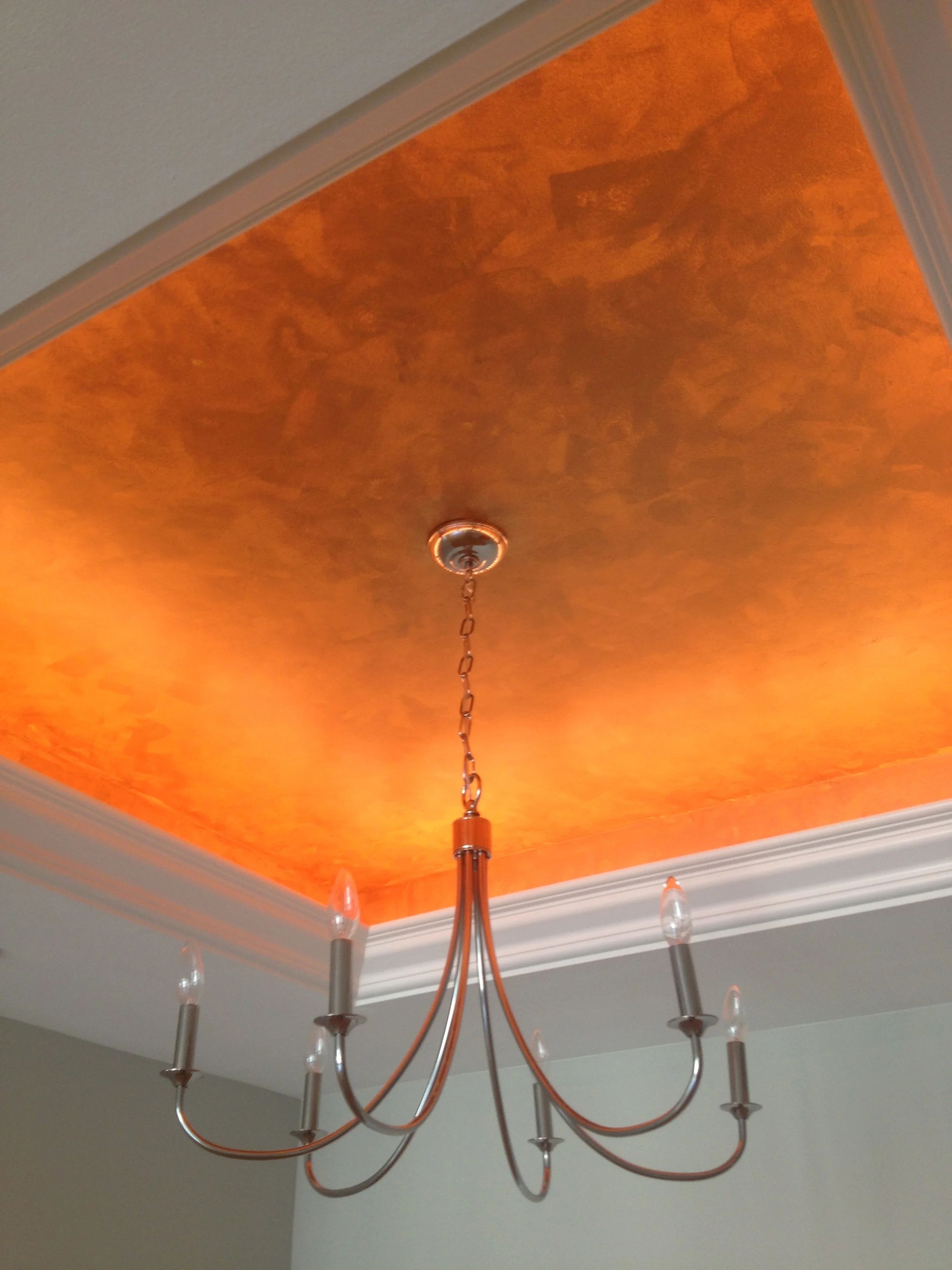  This metallic faux finish with strong orange undertone was created by tinting the base color darker with each pass of the application. The simple light fixture allows for a view and lighting inside the opening features this specialty ceiling cove. 
