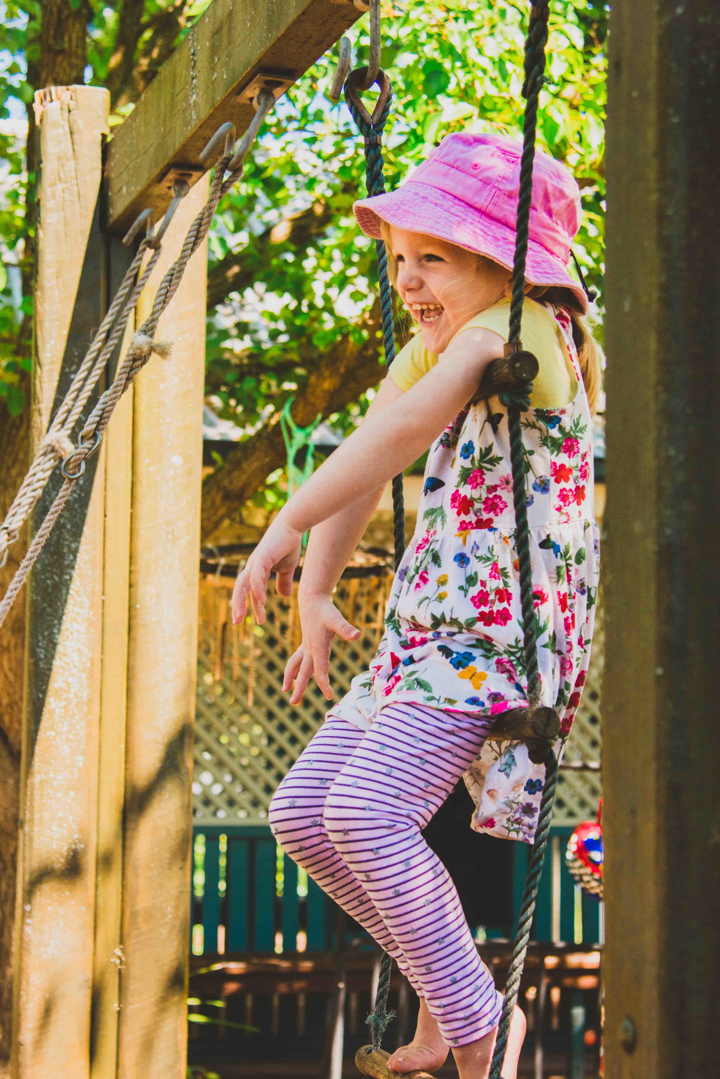 Little girl in pink hat laughing with joy on rope ladder