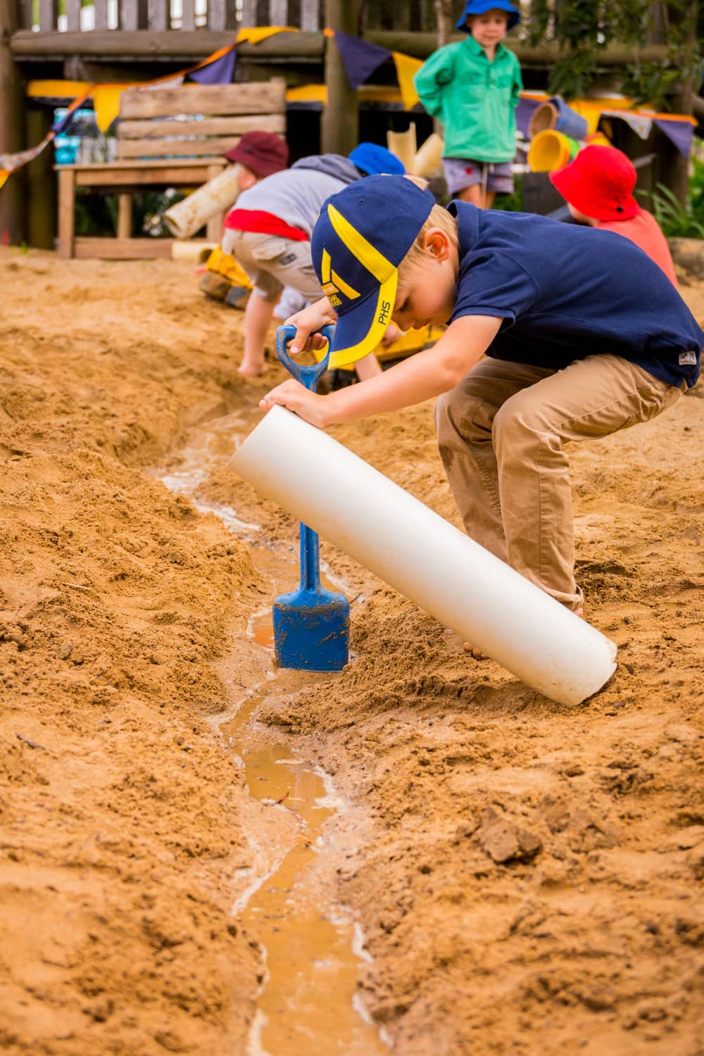 Children playing in kindy sandpit with spades and white pipe