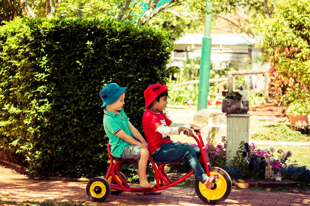 Boy giving his friend a ride on a red tricycle