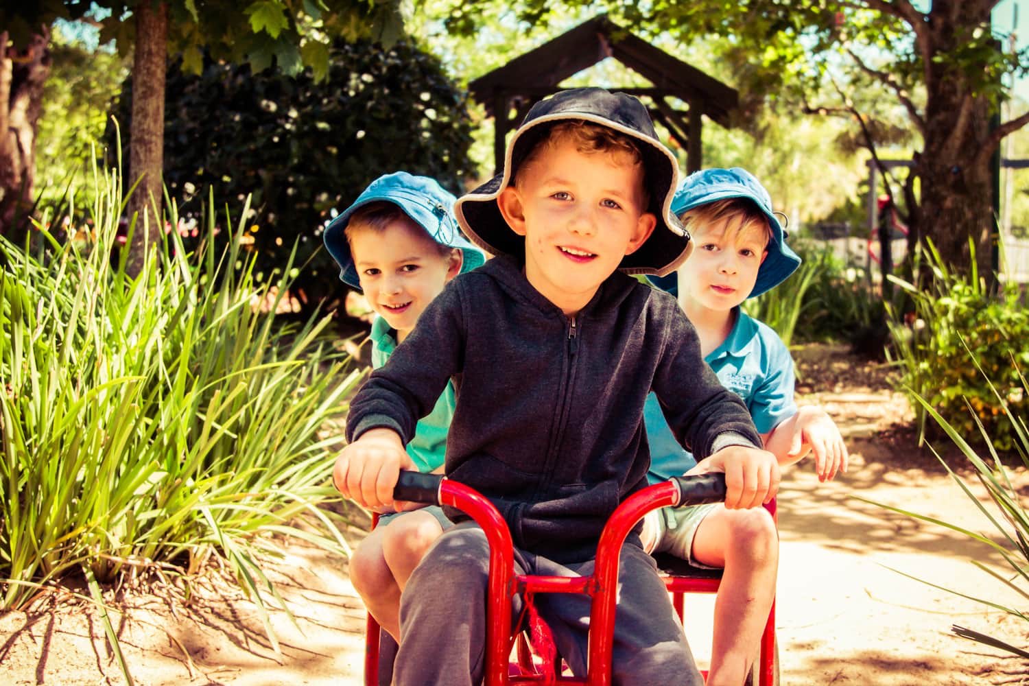 Three boys on red tricycle in Chiselhurst Kindergarten garden