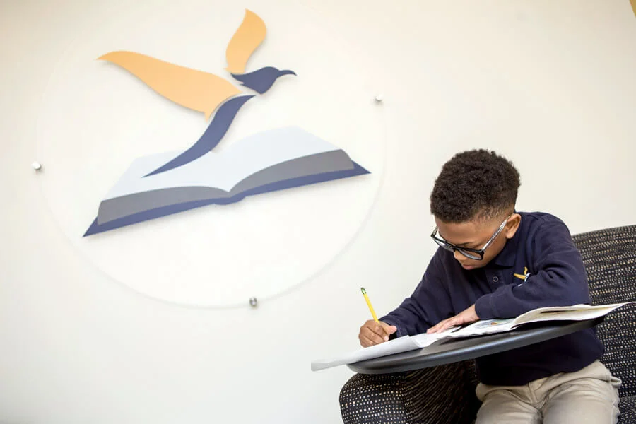 A student sitting, working on a writing assignment, with the Purpose Prep logo on the wall behind him.