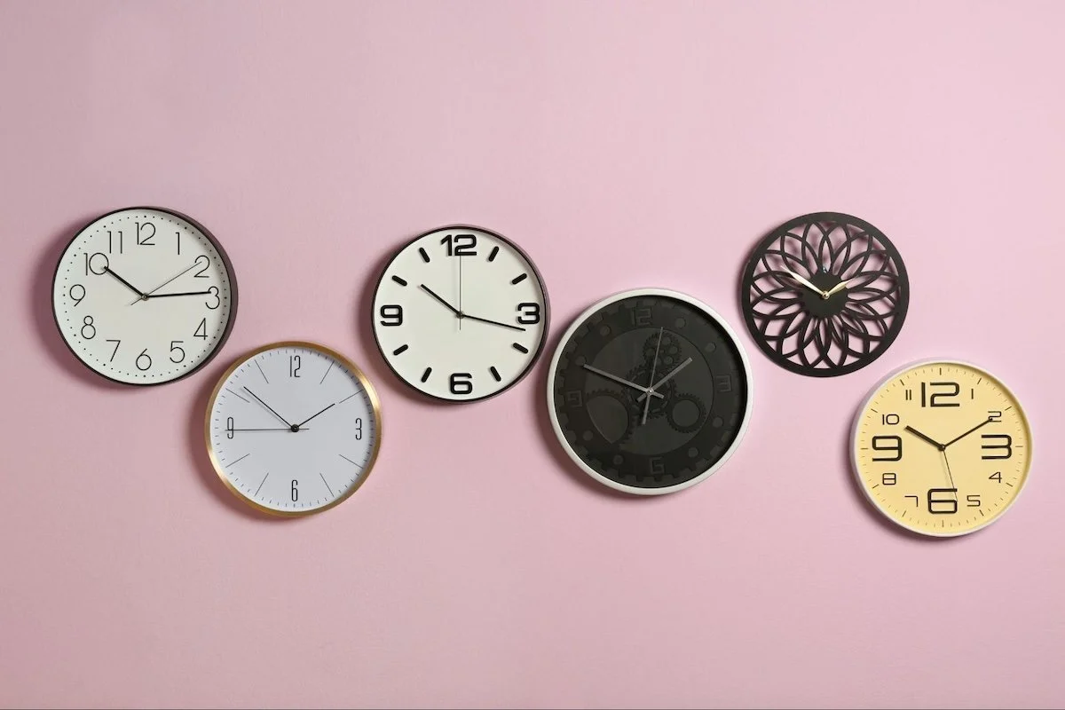 Six clocks in a variety of styles hang on a pink wall.
