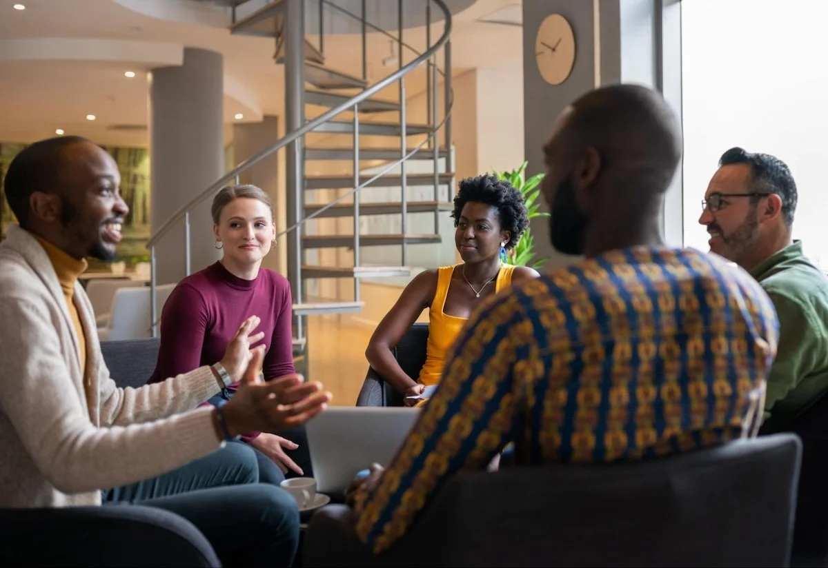 Five people sit in a circle in a modern office building. One man is animatedly talking.