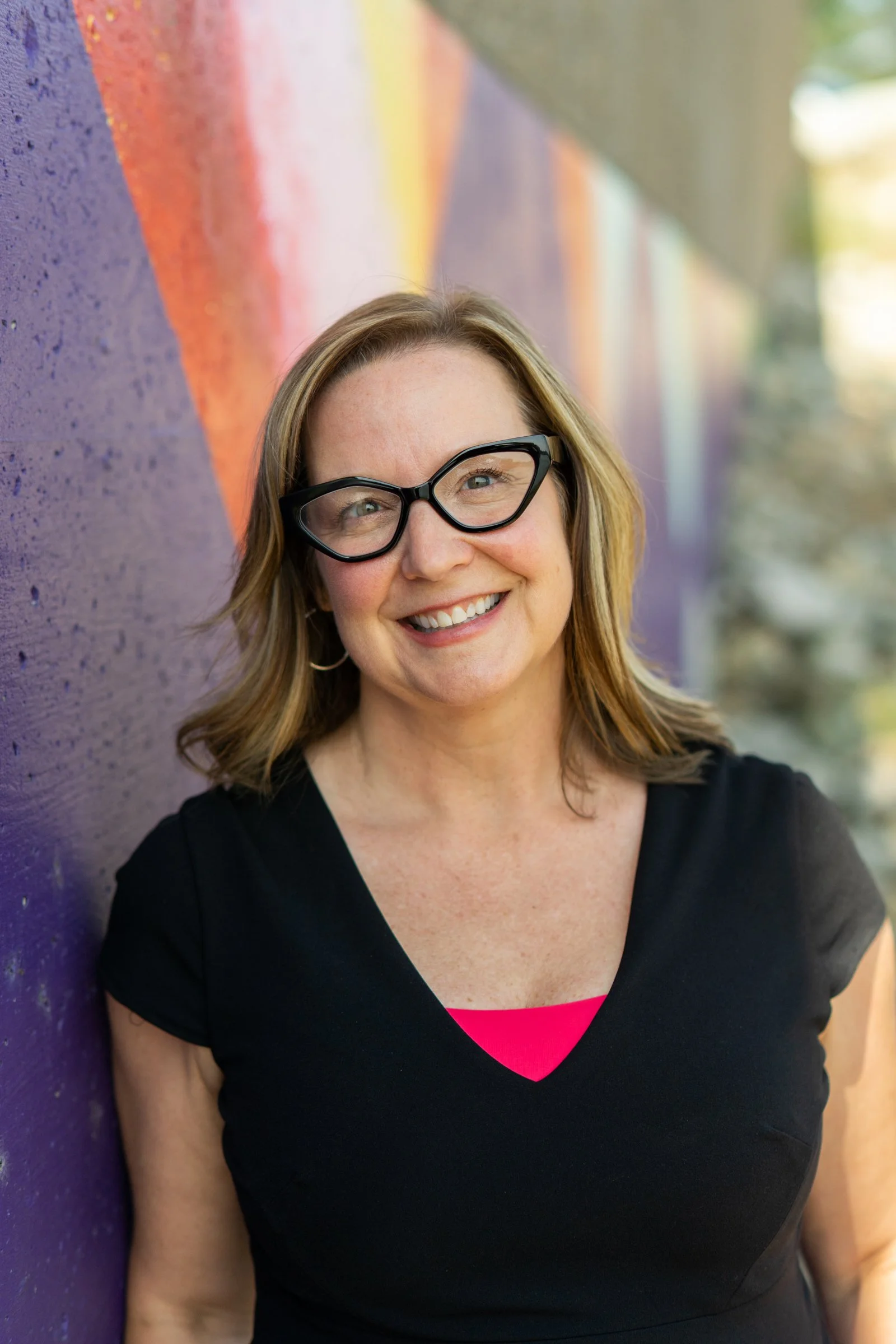Stacy Van Gorp, See What I Mean co-founder and philanthropy consultant, smiles in front of a colorful mural