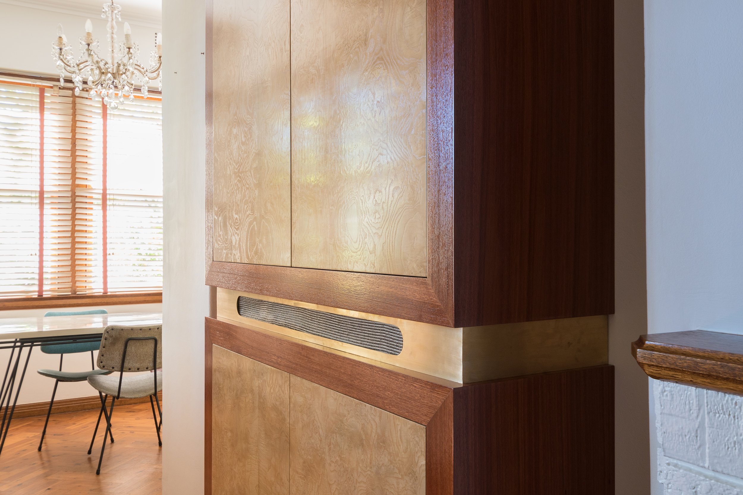 A detailed shot of the media cabinet, showcasing the burl veneer with its swirling movement and rich texture. Brass details on the cabinet add a touch of elegance, while the clever design conceals the TV and stereo, as well as the fridge from the op