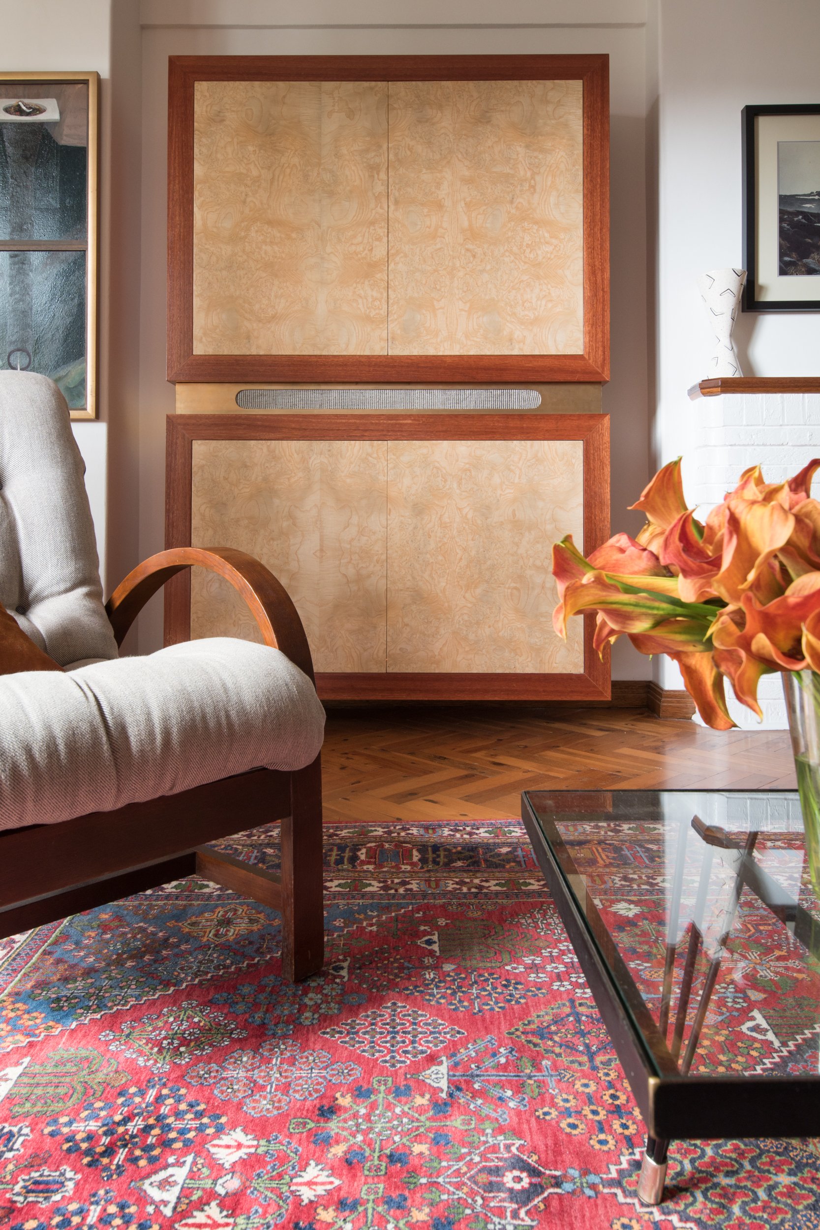 A view of the new media cabinet, crafted from distinctive burl veneer that highlights the swirling movement in the timber. The cabinet is complemented by the client's reupholstered vintage furniture and art collection, blending heritage character wi