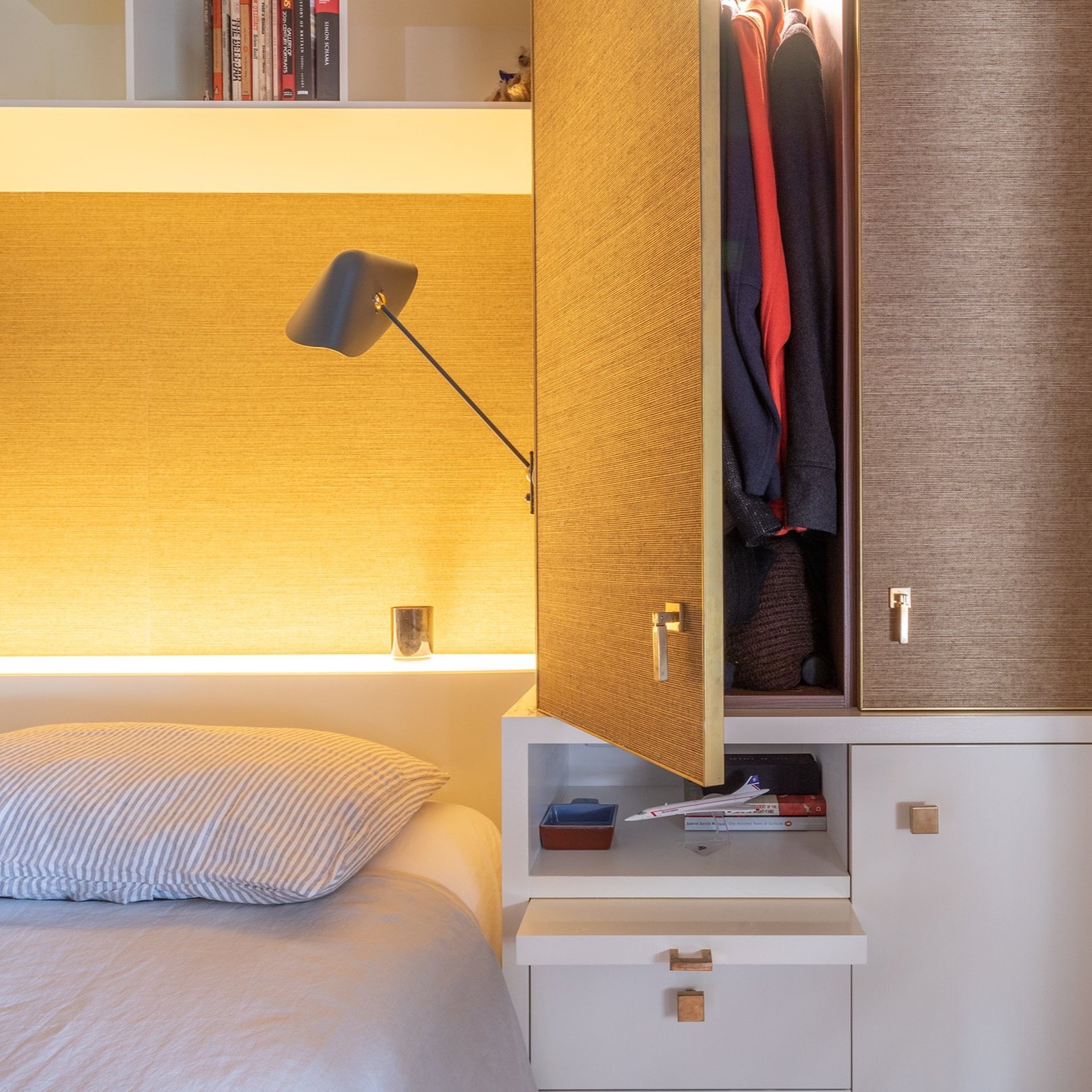 A detailed shot of the robe cabinets in the bedroom, featuring doors finished in grass paper wallpaper with brass edging. Brass cabinet pulls complement the elegant detailing, while French wall sconces add a touch of refinement. The pull-out bedside