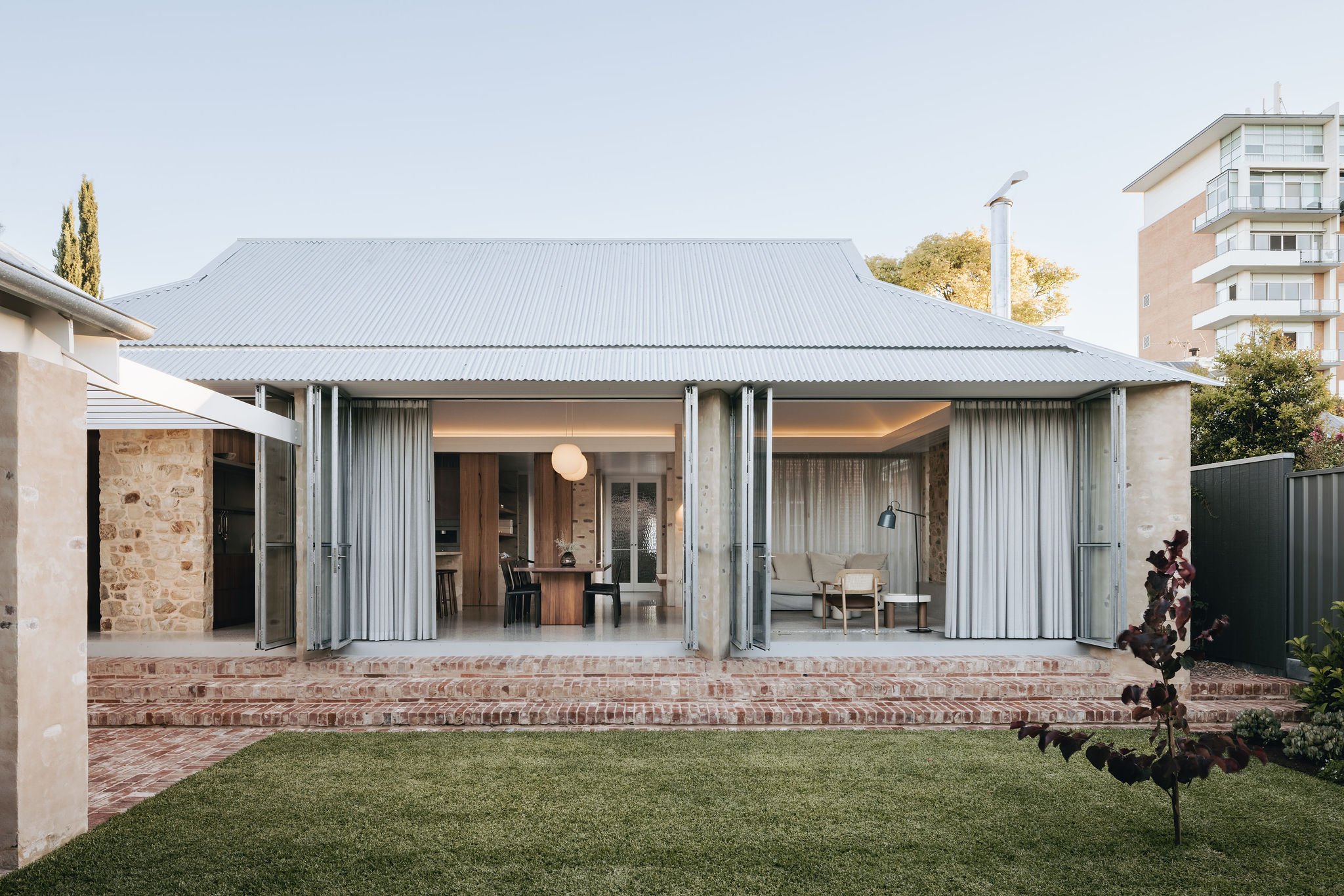 The rear elevation of the house features a Dutch gable roof form that echoes the original frontage, tying the contemporary design to the heritage elements. Large north-facing galvanised doors flood the spacious living areas with natural light and bi