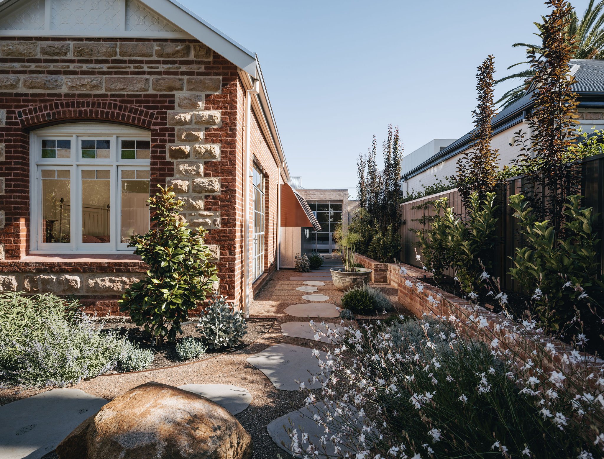 Side view of a restored Adelaide villa with Adelaide Hills sandstone, featuring stepping stones leading to a modern rear addition. The traditional facade transitions into the contemporary extension, blending both architectural styles.