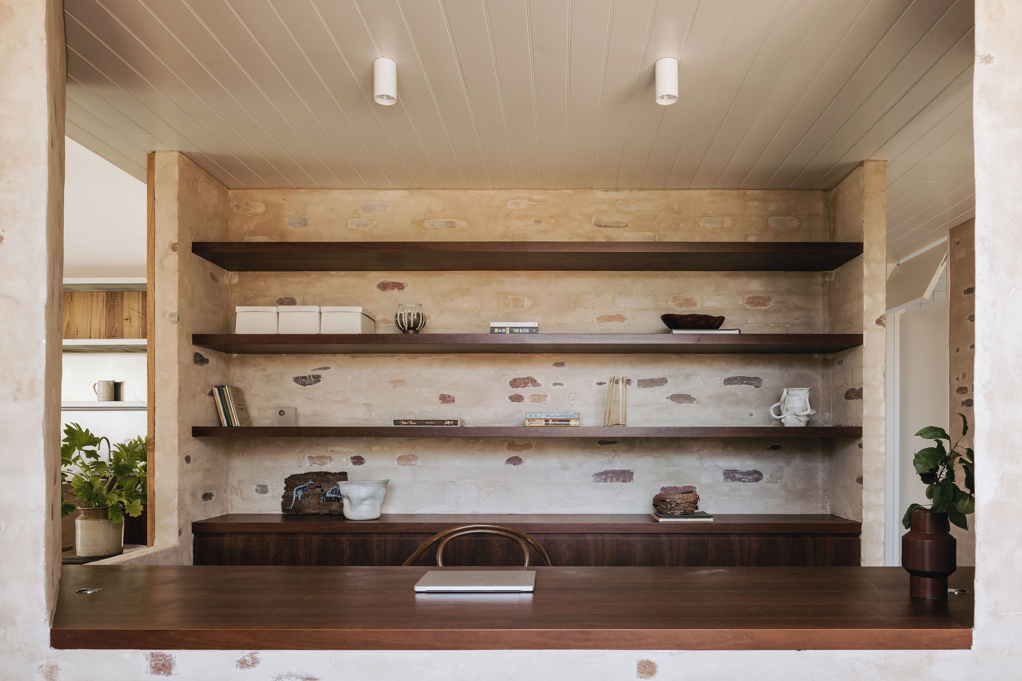 View into the study, showcasing built-in study desk, shelves, and joinery with Australian veneer detailing. The space features bagged brickwork, a timber matchboard ceiling, and a peep hole through to the kitchen, creating a visual connection betwee
