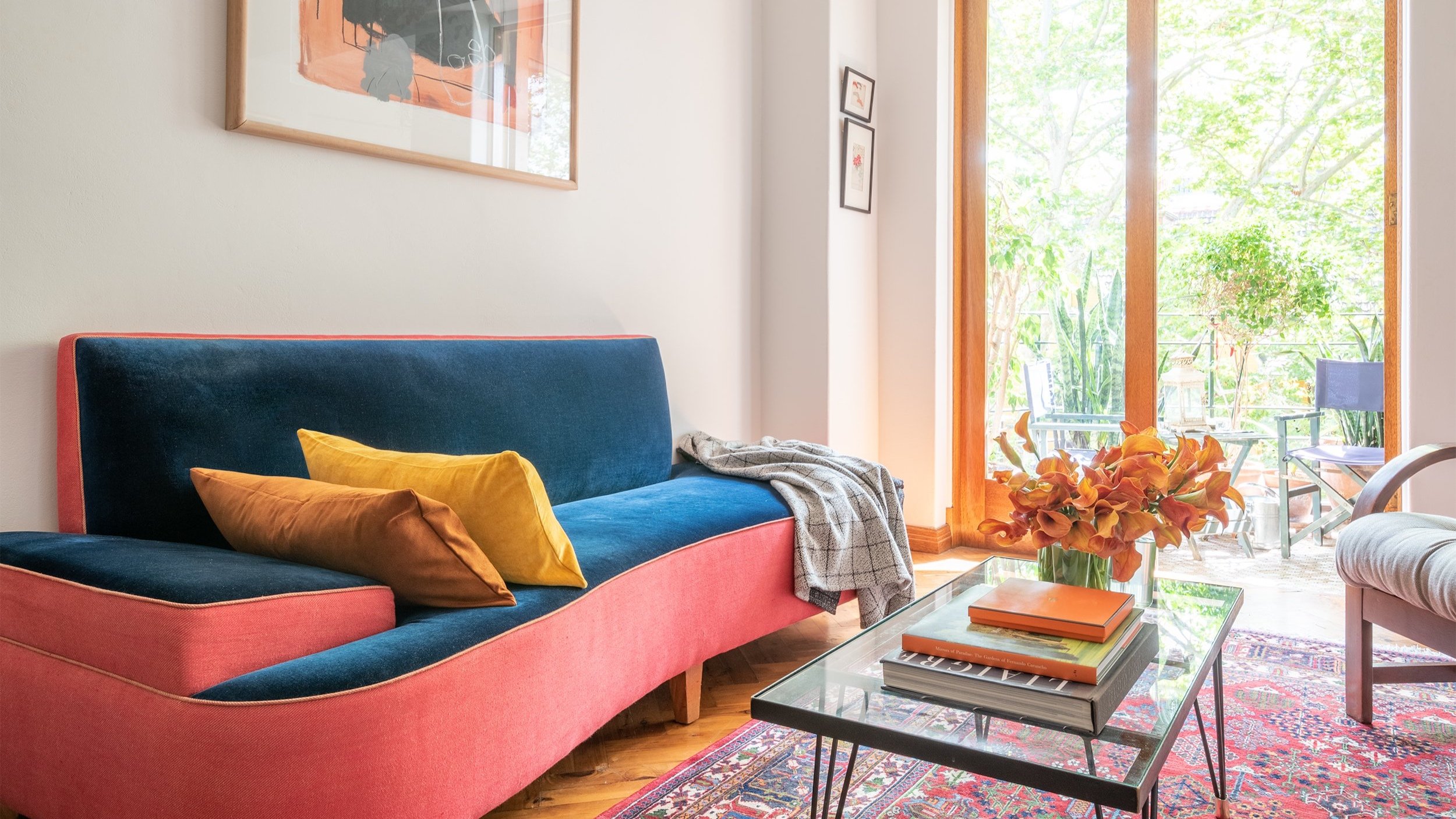 A perspective past the reupholstered sofa, looking through the small curved balcony with its Art Deco railing towards the street tree canopy beyond. This shot captures the blend of vintage interior charm and the urban setting, offering a moment of t