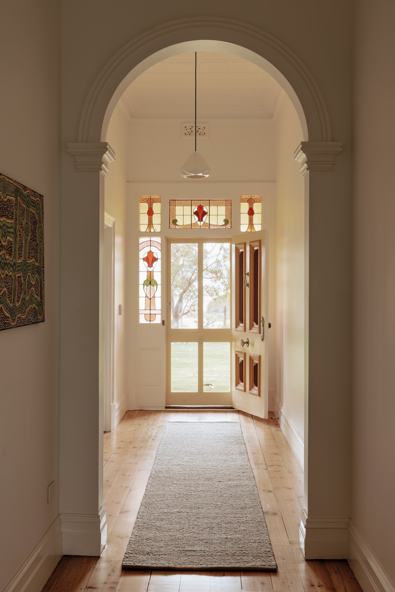 A view down the hallway towards the old front door, where a new arch, crafted with traditional plaster moulds, adds a graceful touch. New porcelain pendant lights, alongside the original timber floors, bring elegance to the space, while the preserve