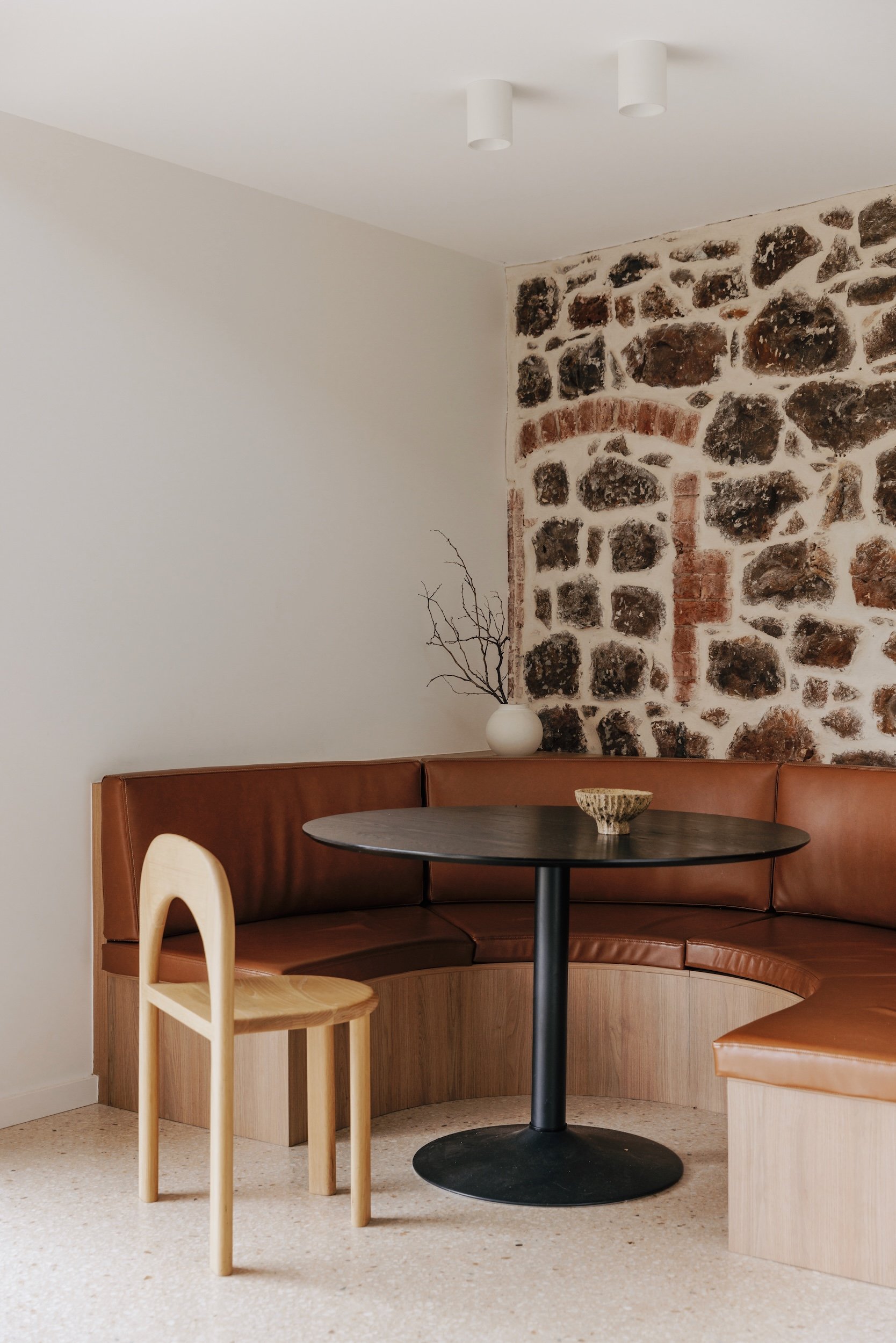A view of the breakfast nook with curved banquette seating, nestled against the old stone wall of the original house, offering a comfortable and inviting spot for meals. The modern seating contrasts beautifully with the historic stone wall, highligh