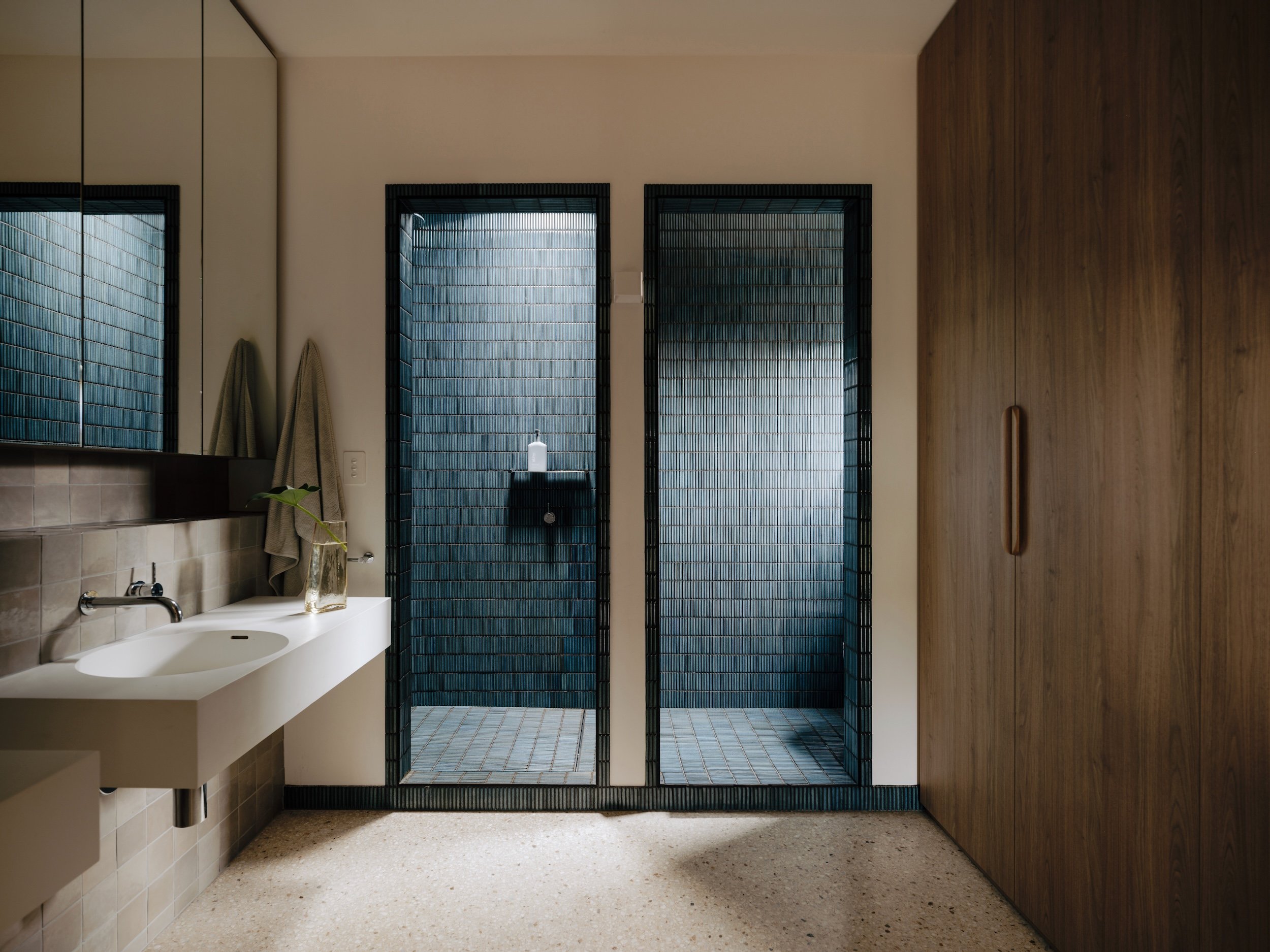 A view of the ensuite, featuring a relaxed open feel that flows from the adjoining robe space. The polished concrete floor extends from the new additions, with tiles to the hob selected to complement the floor's colour. Skylights and windows in the