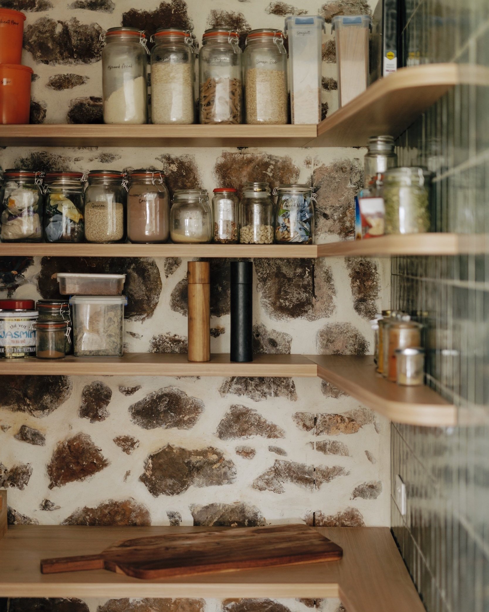 A detailed shot of the pantry, fitting neatly between the new kitchen additions and the old stone wall of the house, enhancing the charm of this utilitarian space. Open shelves provide easy access to pantry items, while a small benchtop offers room