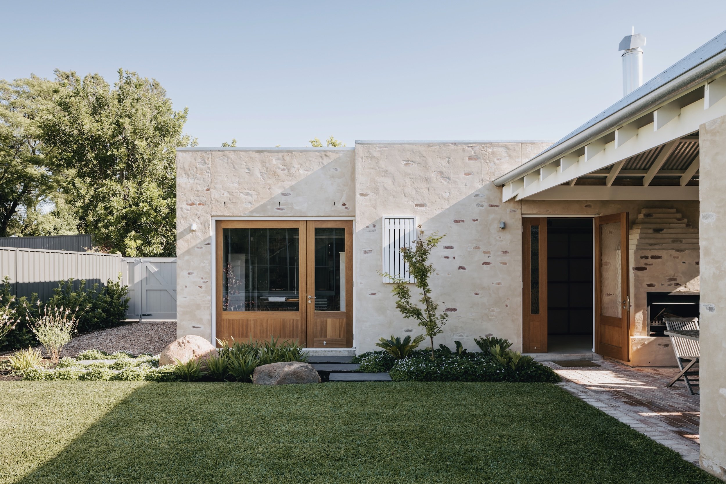 View across the back lawn to the garage outbuilding, showing the bagged brickwork and large timber doors that open on the garden. The outdoor living space is designed to extend the home’s connection to the outside, providing a peaceful retreat that