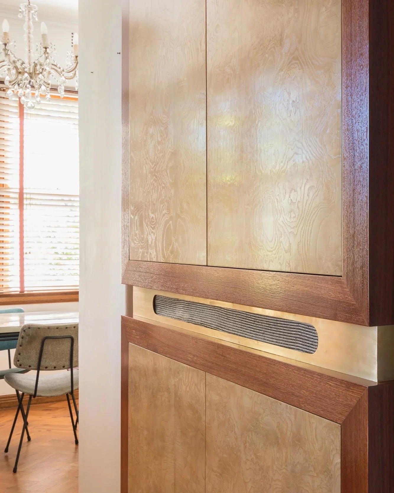  A detailed shot of the media cabinet, showcasing the burl veneer with its swirling movement and rich texture. Brass details on the cabinet add a touch of elegance, while the clever design conceals the TV and stereo, as well as the fridge from the op