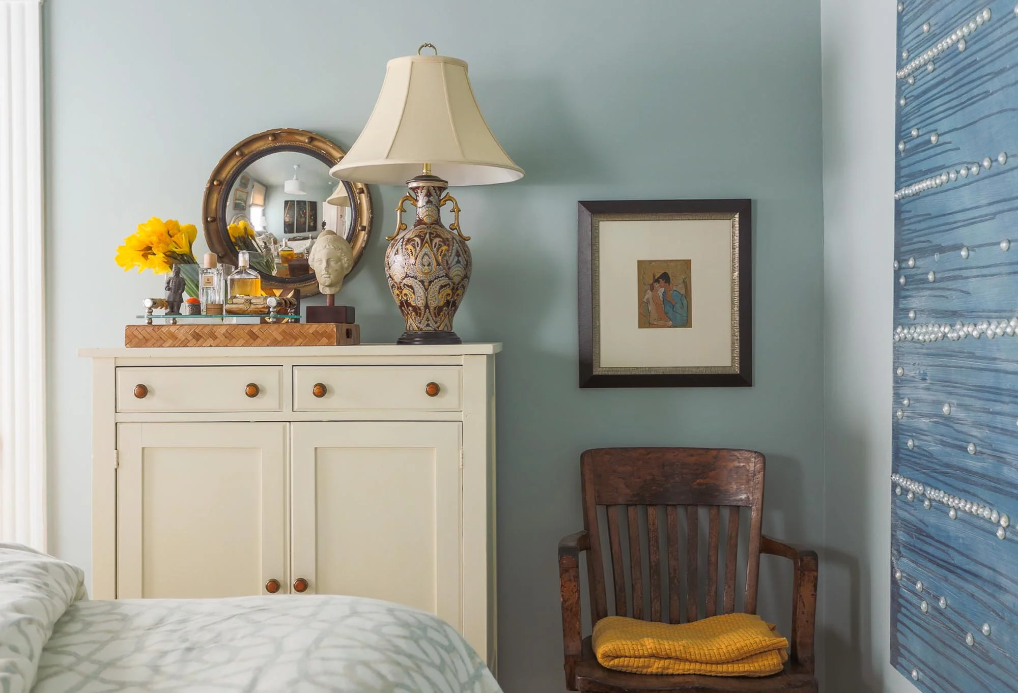 Bedroom interior with single hair, lamp shade and other decorations on the top of the white wooden dresser.