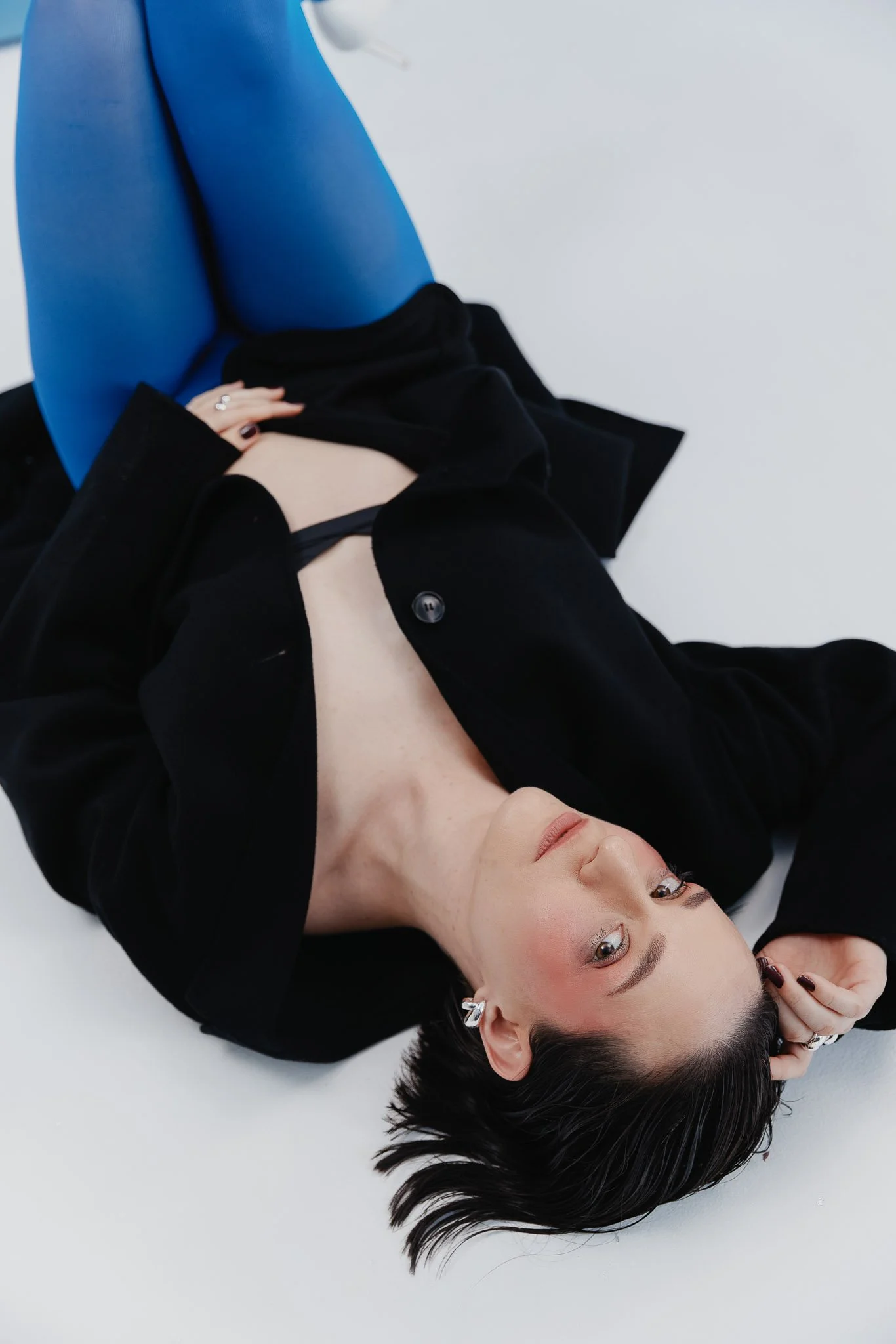 Headshot of a woman with natural makeup, smiling in a studio, wearing a black top blazer model blue leggings workshop model london