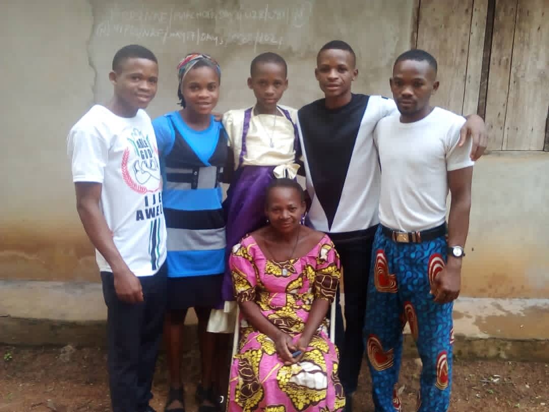Emmanuel (2nd from right) with his mom (center, front) and four of his seven siblings; their house is in the background.