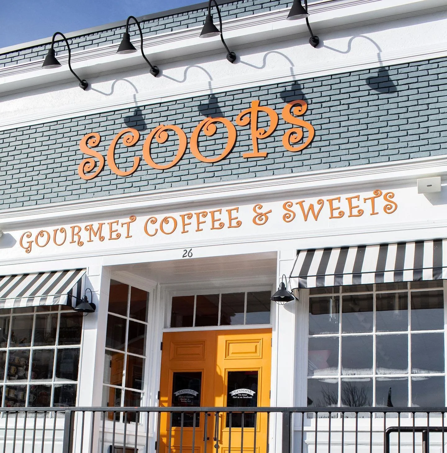 Storefront of 'Scoops Gourmet Coffee & Sweets' with a retro-looking orange door and striped awnings.