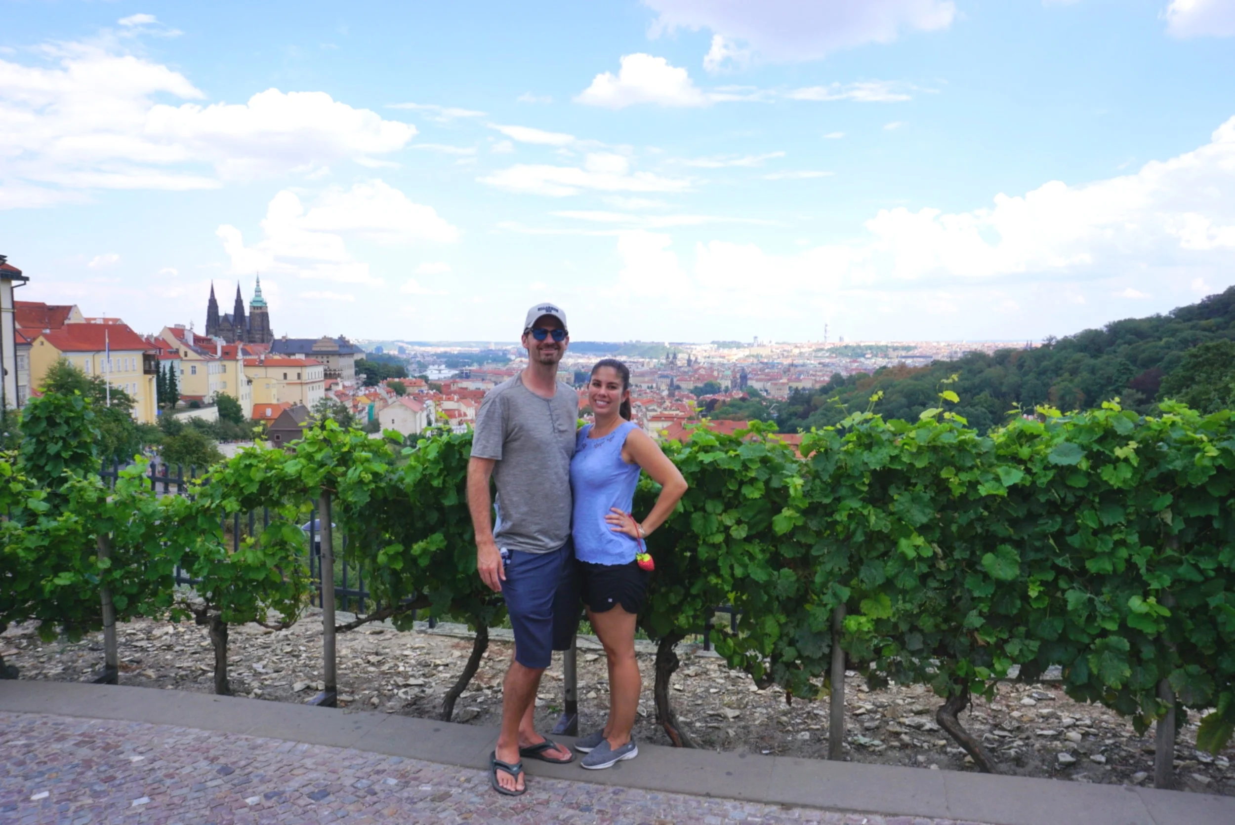Kelly and Matt of Boldly Go Travel stand for a photo with a majestic view of Prague in the background. boldlygotravel.com