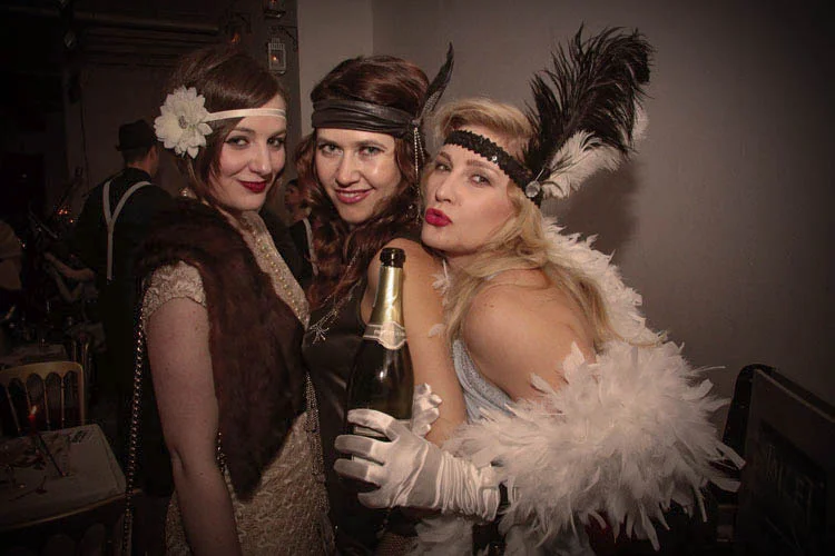 Three women with headbands, boas and Champagne
