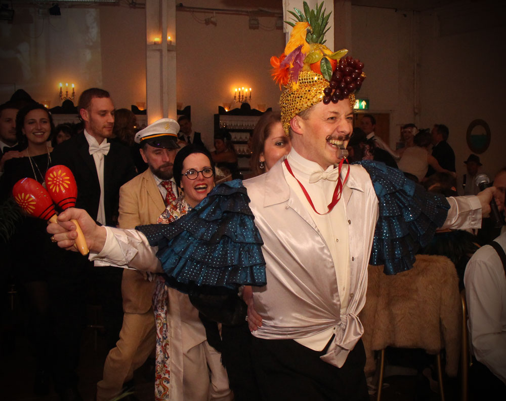 Champagne Charlie leading a conga line with a fruit headdress