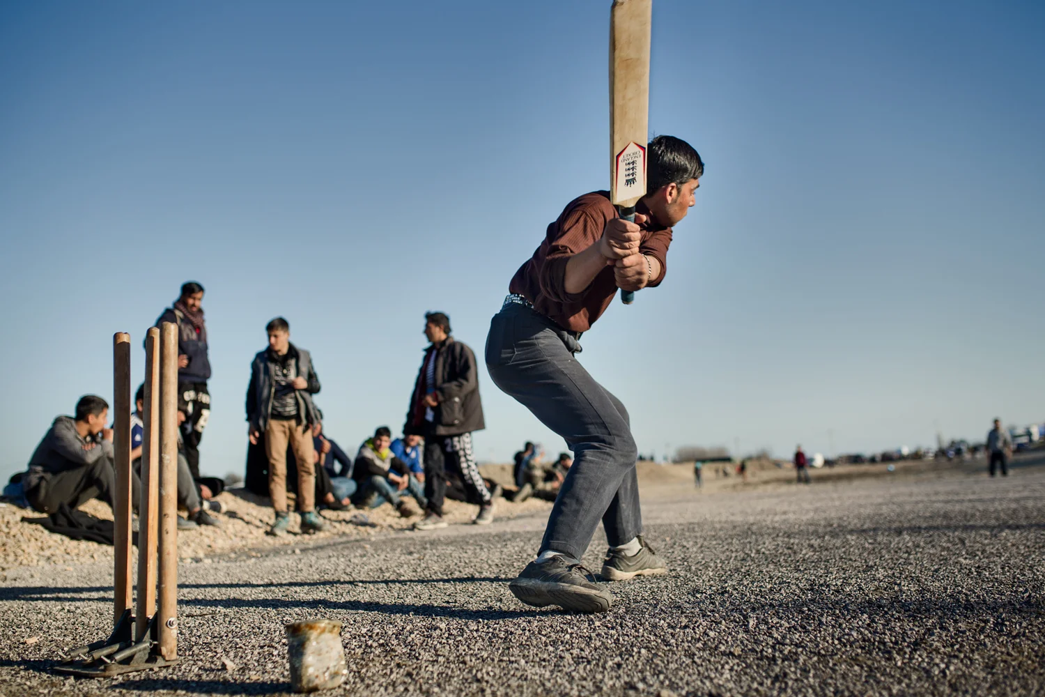  A young Afghan boy gets ready to hit a cricket ball as the sun sets in the Calais Jungle, France, March 2016. Sport in refugee camps is always an opportunity to escape from routine and revive happy sensations. 