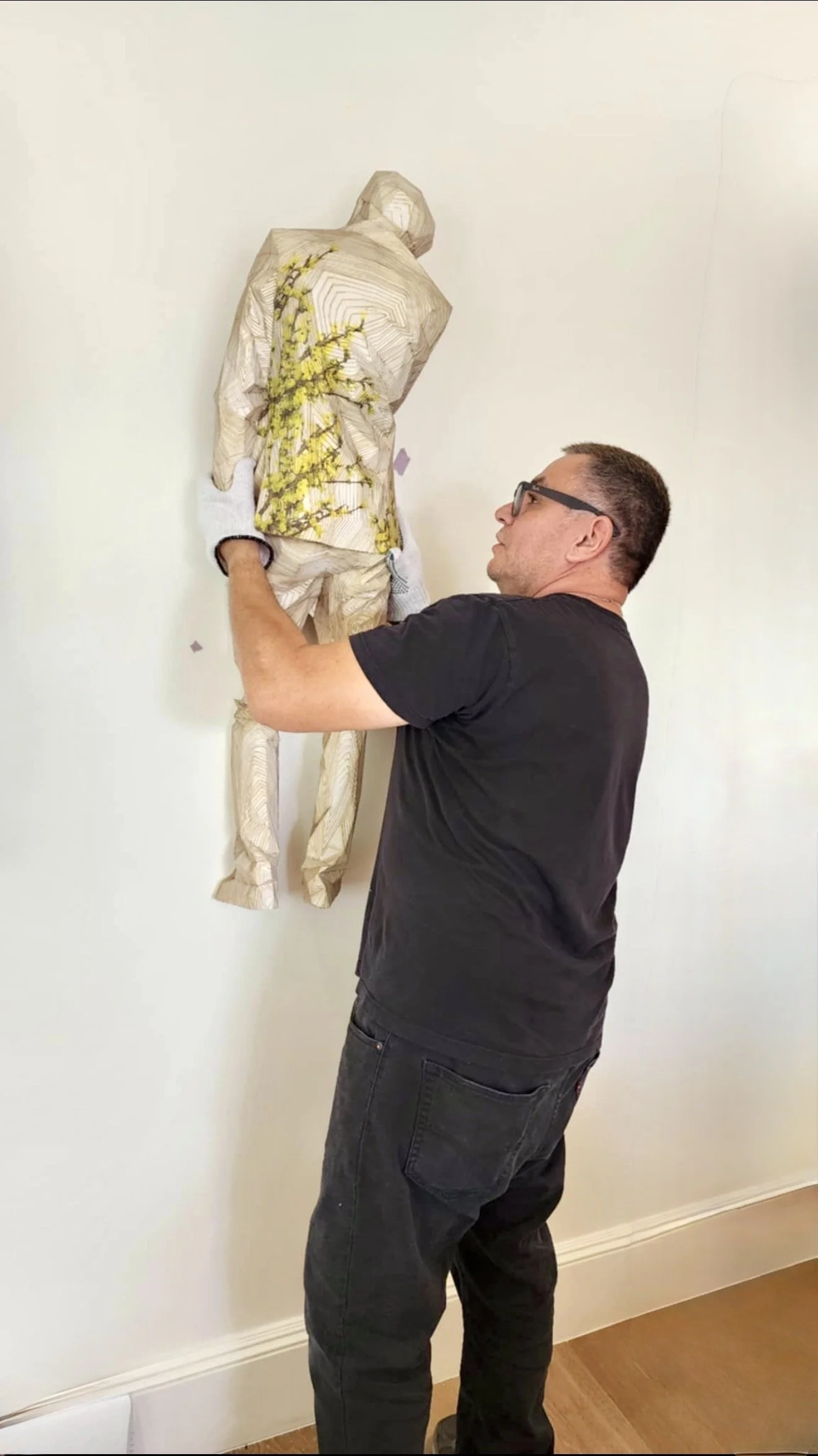 Man handling a wooden sculpture of a woman in a standing pose on a wall.