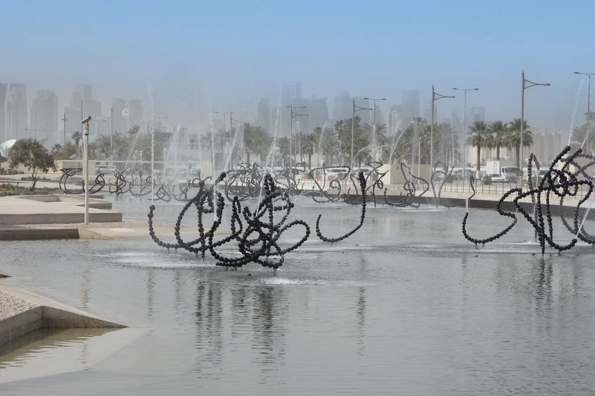 Fountain echoing Arabic script with skyscrapers in background