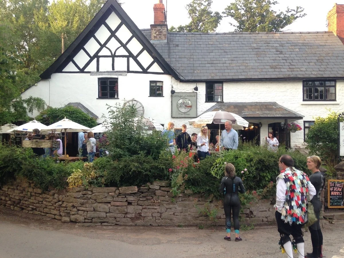 Whitewashed cottage pub with colourfully dressed people standing around