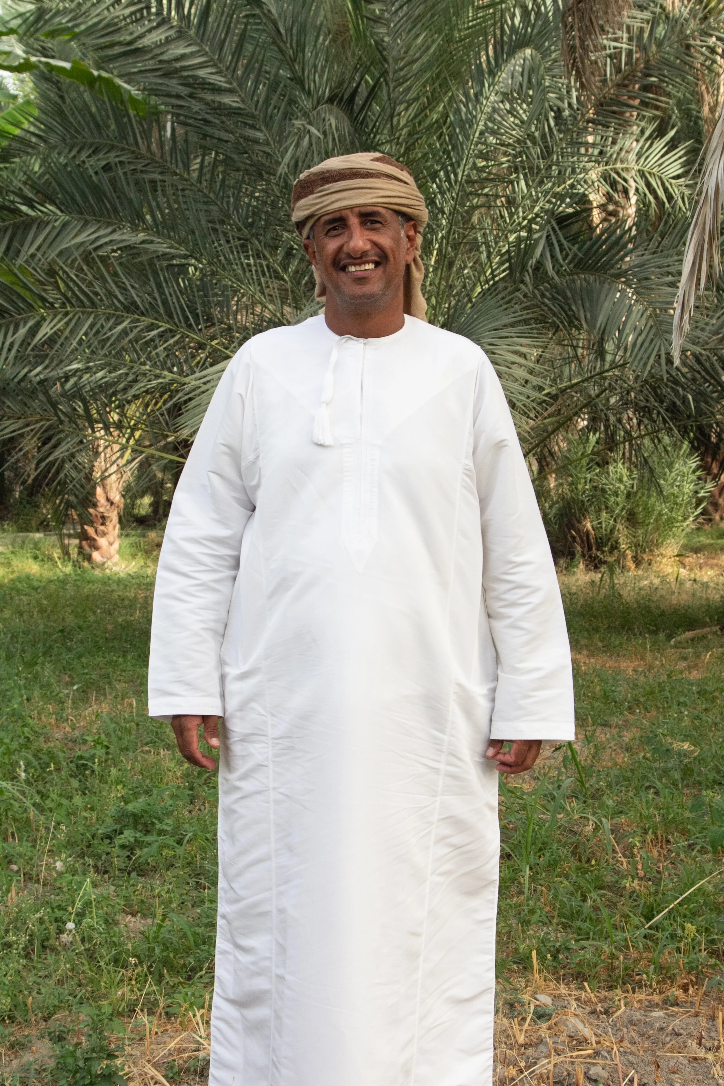 Standing man wearing white galabaya and turban against palm-tree