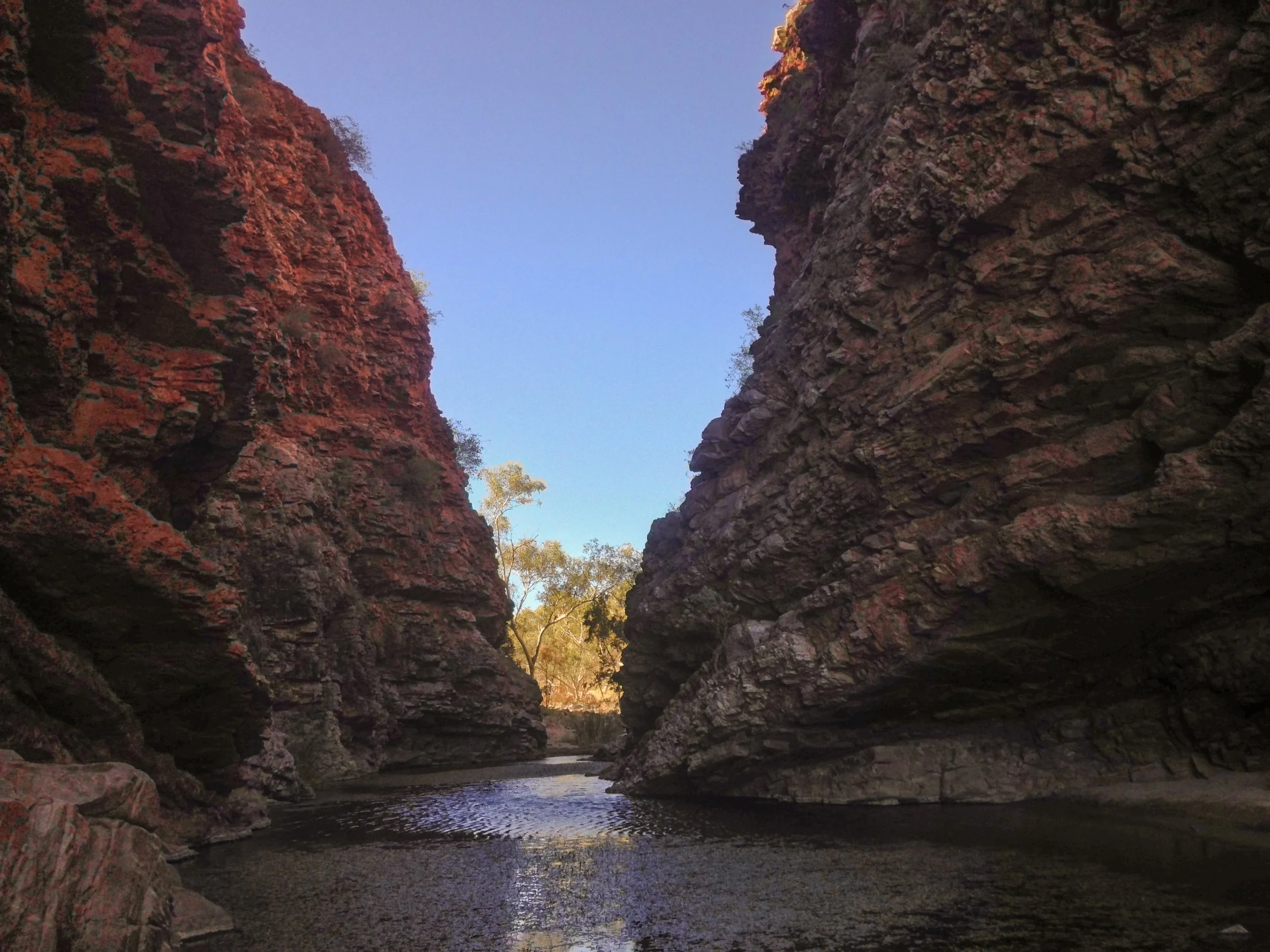 Two sloping red cliffs almost meet in a V at water's edge