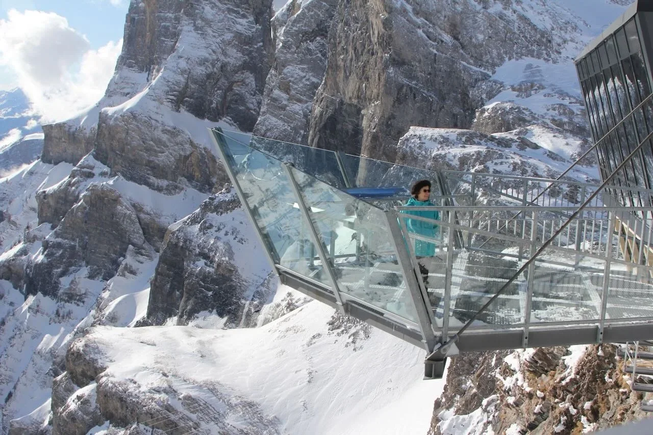 Woman standing on glass overhang against snowy mountain rocks