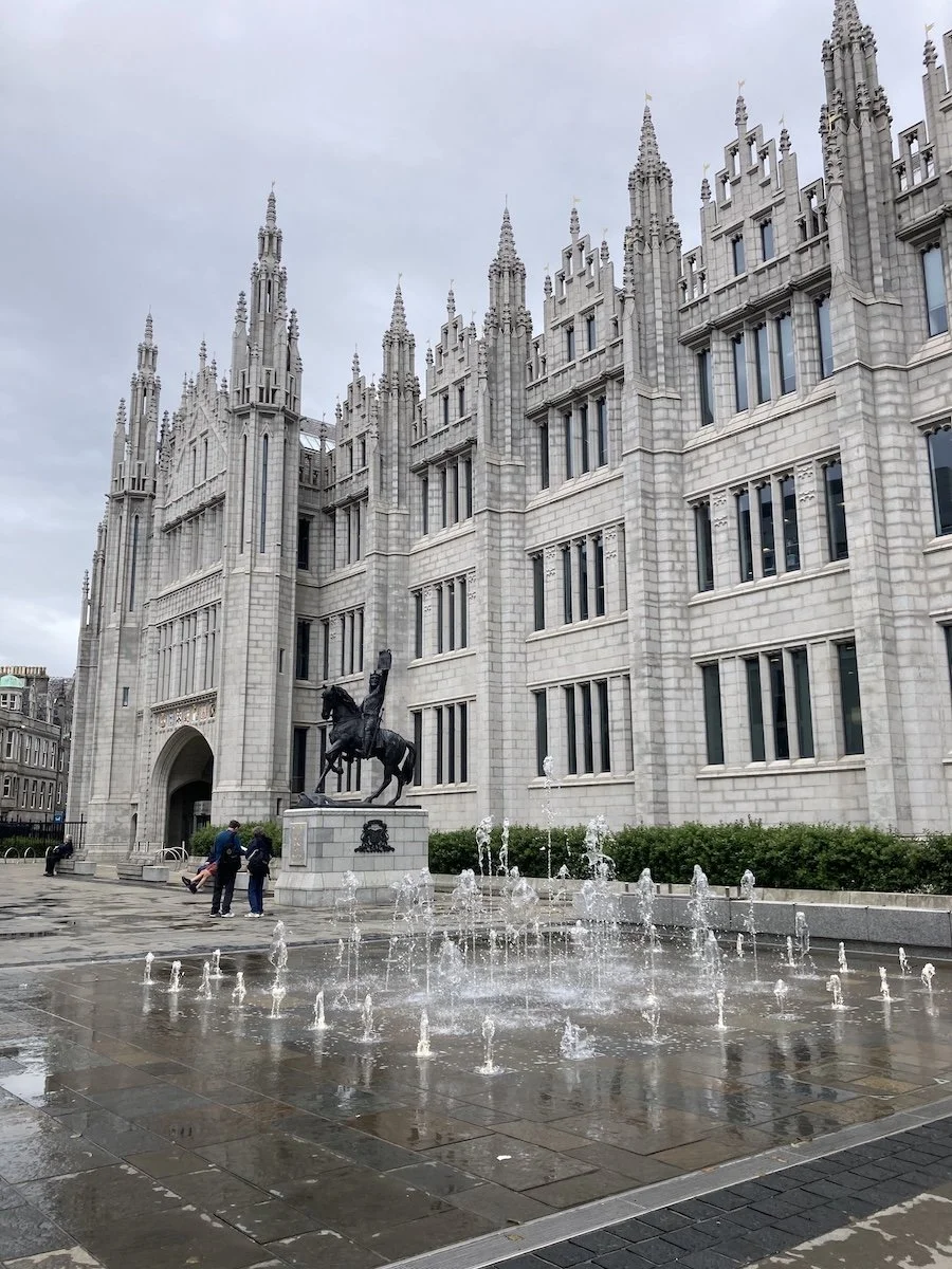 Large grey building with horse statue and fountain