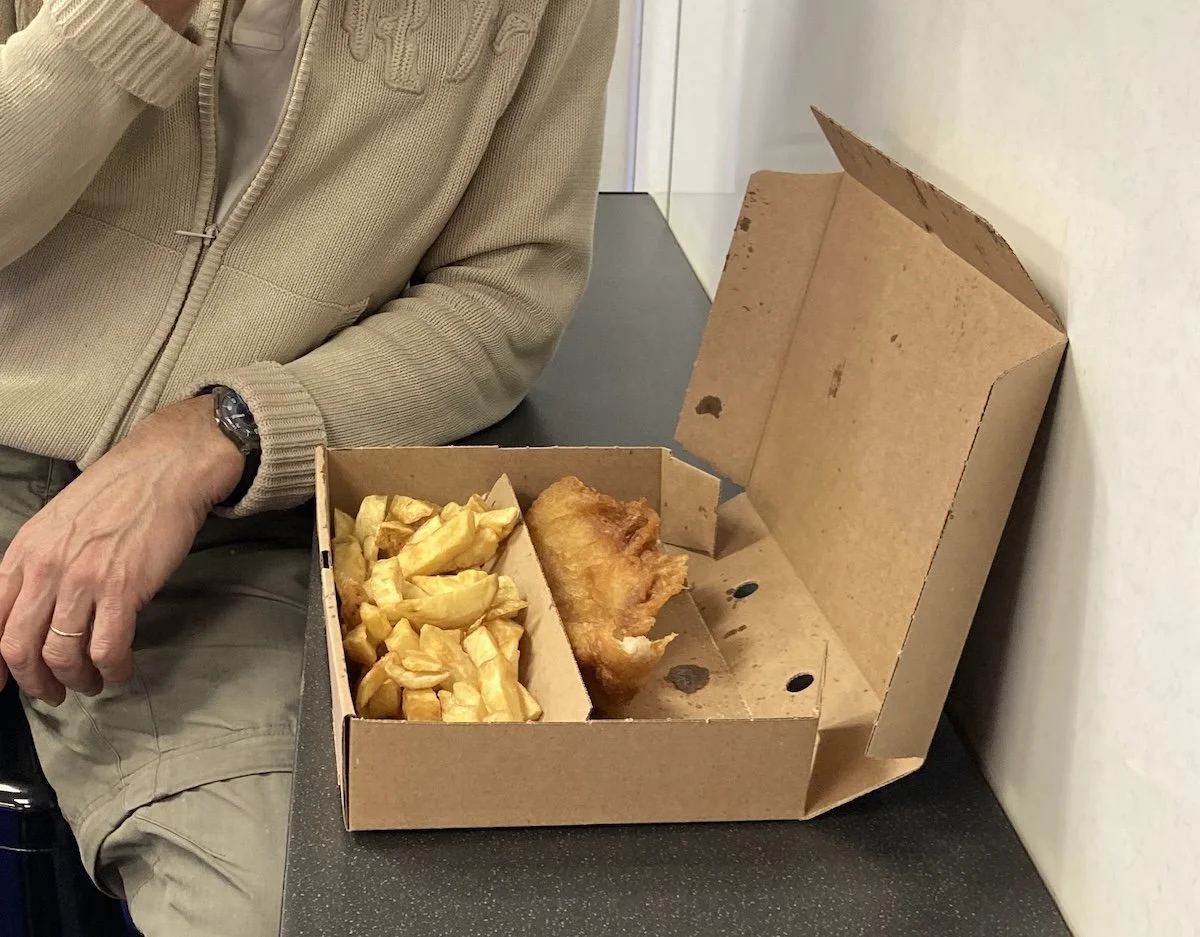 Cardboard box containing chips and fried fish and man's hand