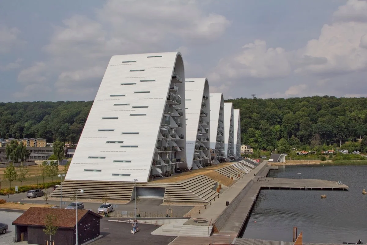 Multistorey building by water with five sloping white roofs to look like waves