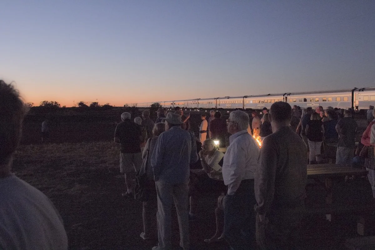 A lot of people standing watching sunrise alongside silvery train