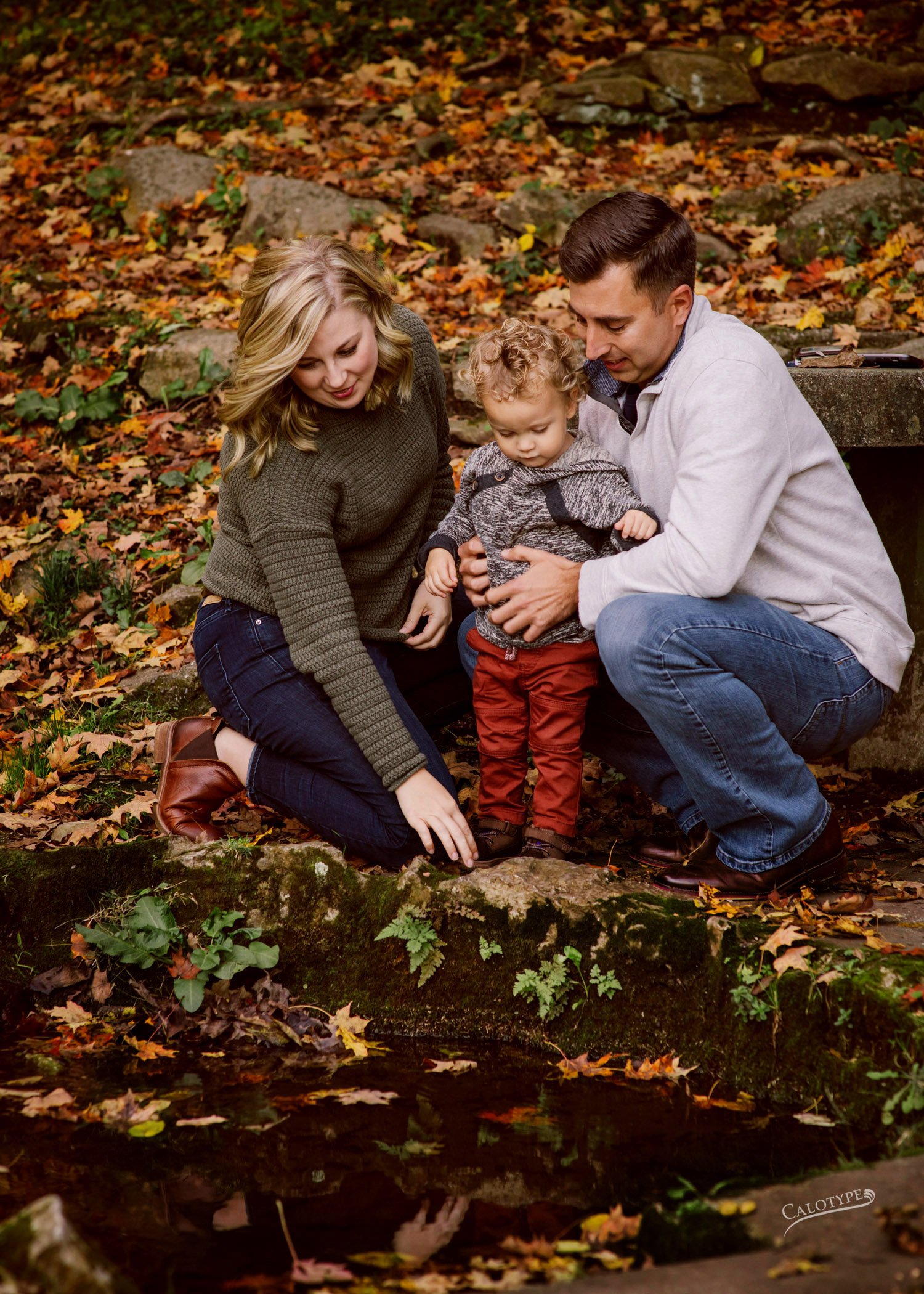 mom, dad and 2 year old peer down at natural spring at Big Spring Park in  Neosho MO