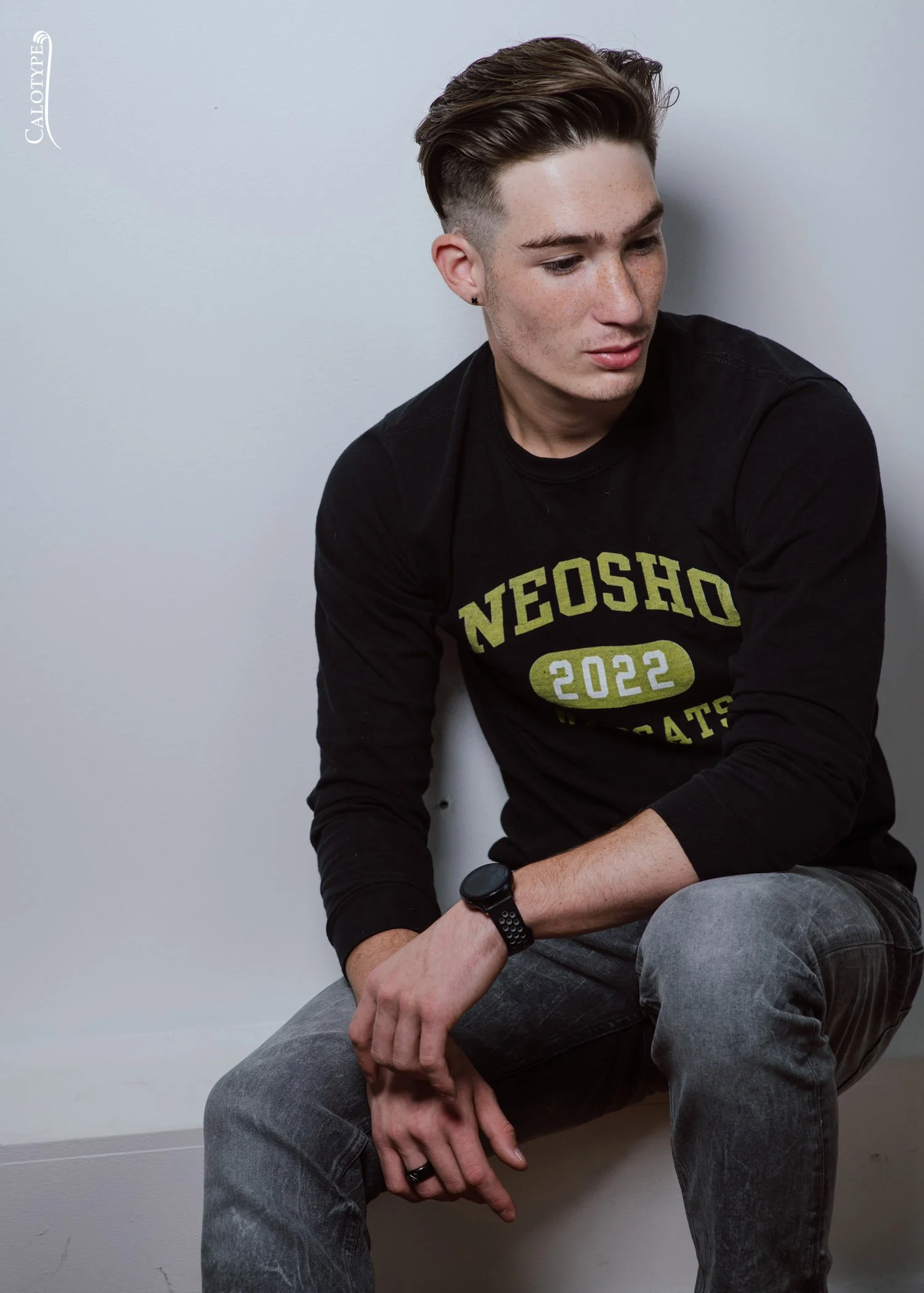 class of 2022 senior sitting on white wall in a studio