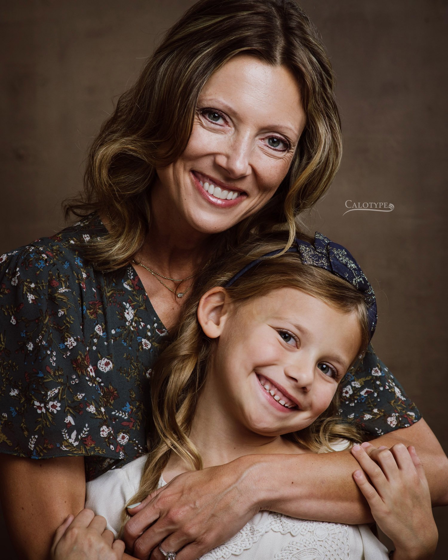 mom with short blonde hair wraps her arms around her 7 year old daughter for a  family photoshoot in the studio