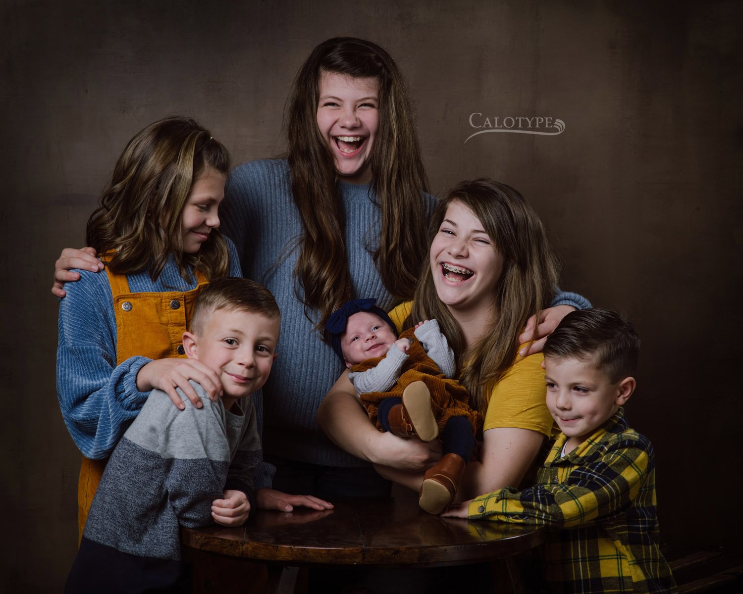 group photo of six cousins laughing at a newborn baby smiling