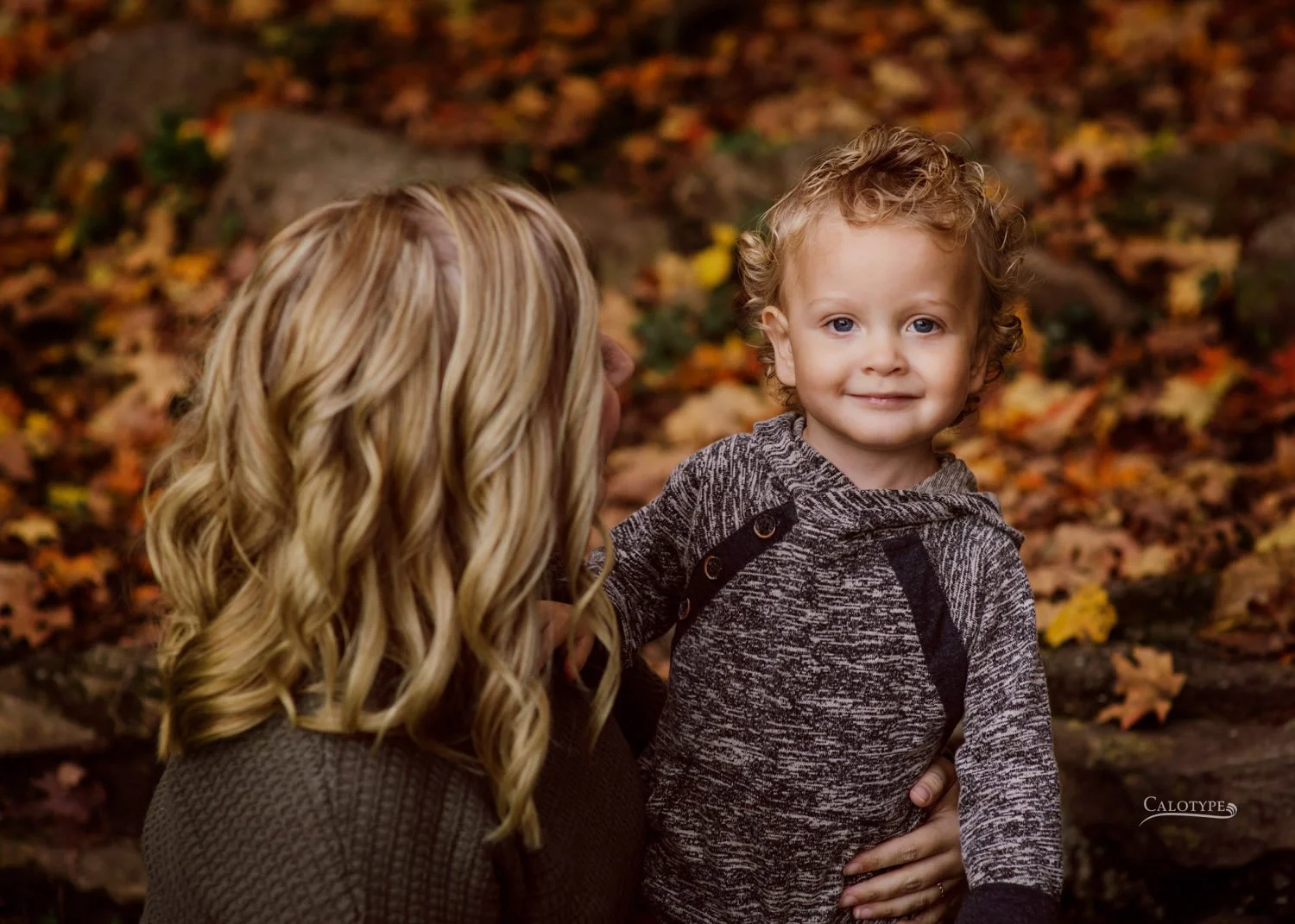 blonde mom holds 2 year old son as he smiles for pictures