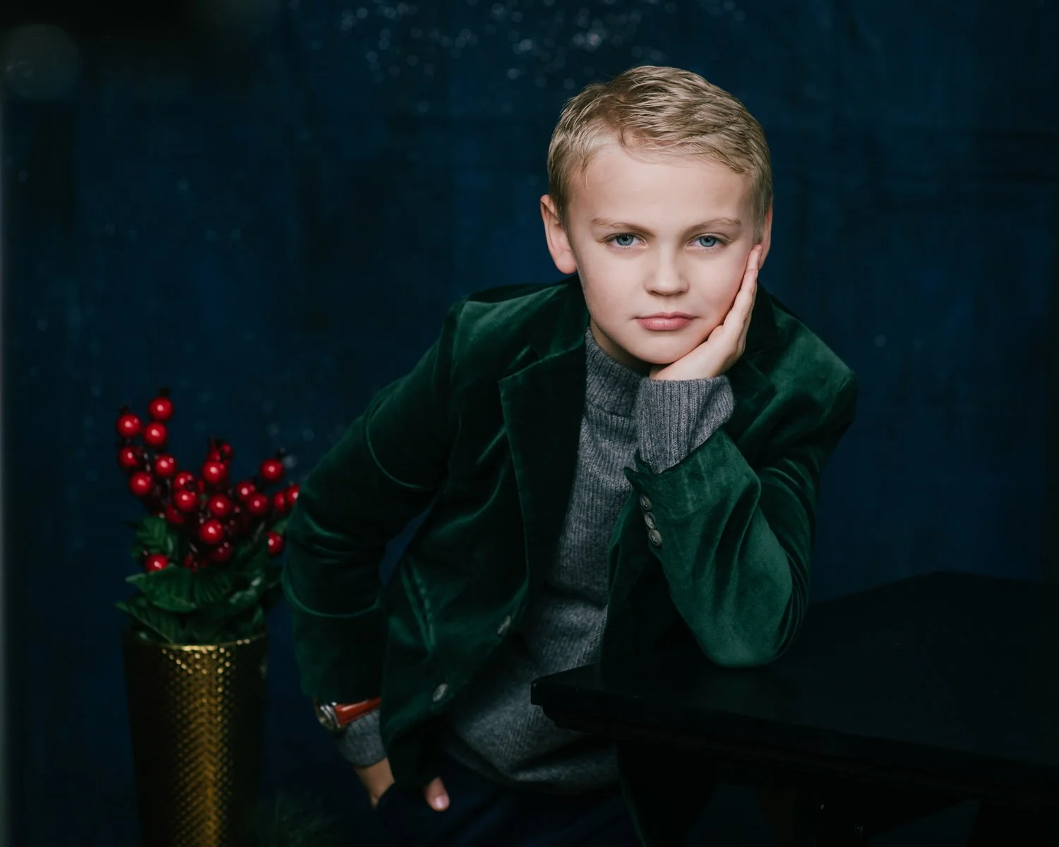 little blonde boy dressed up in green velvet blazer leans on his hand, posing for Christmas pictures