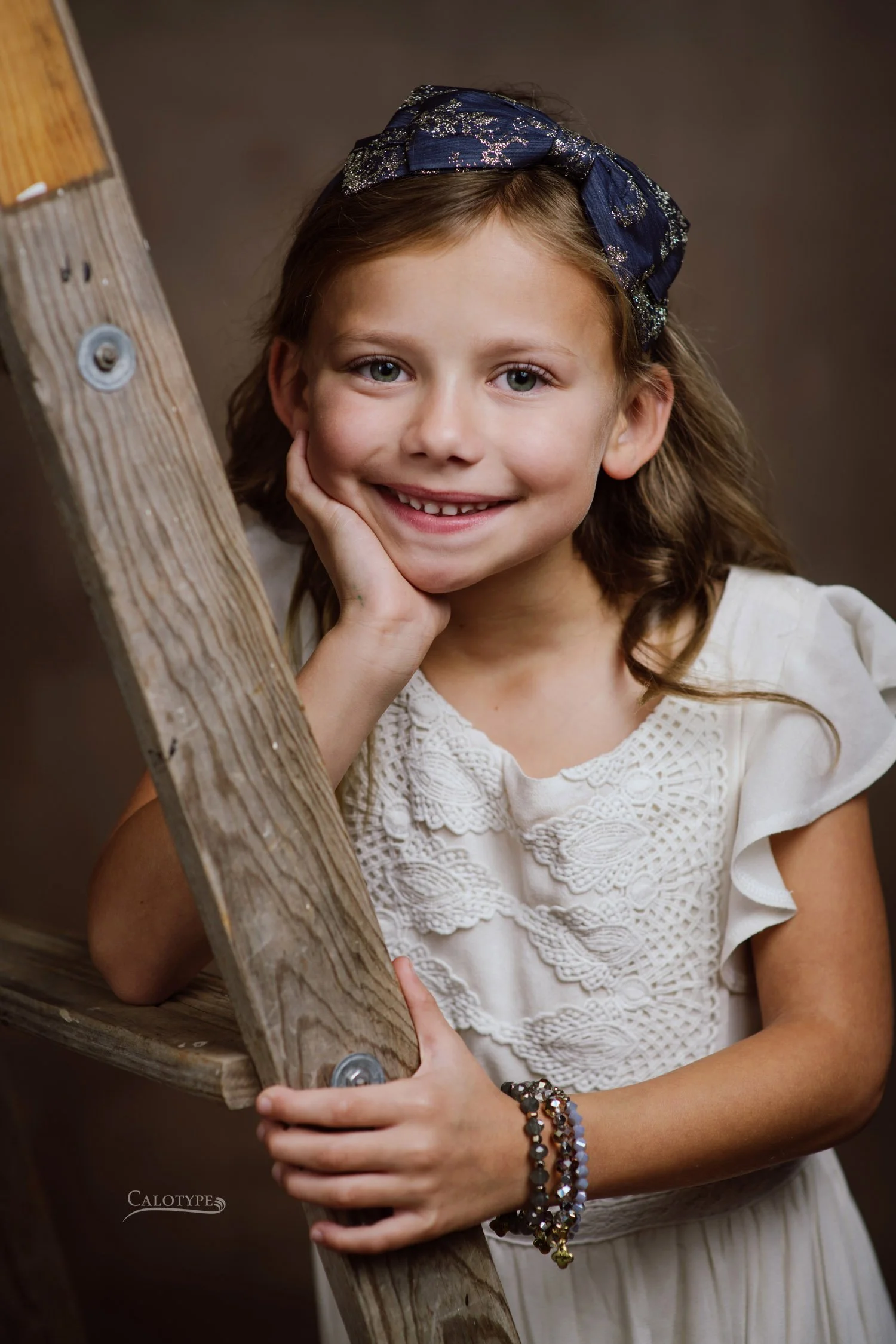 closeup of little girl in cream vintage dress, leaning on an old ladder for pictures