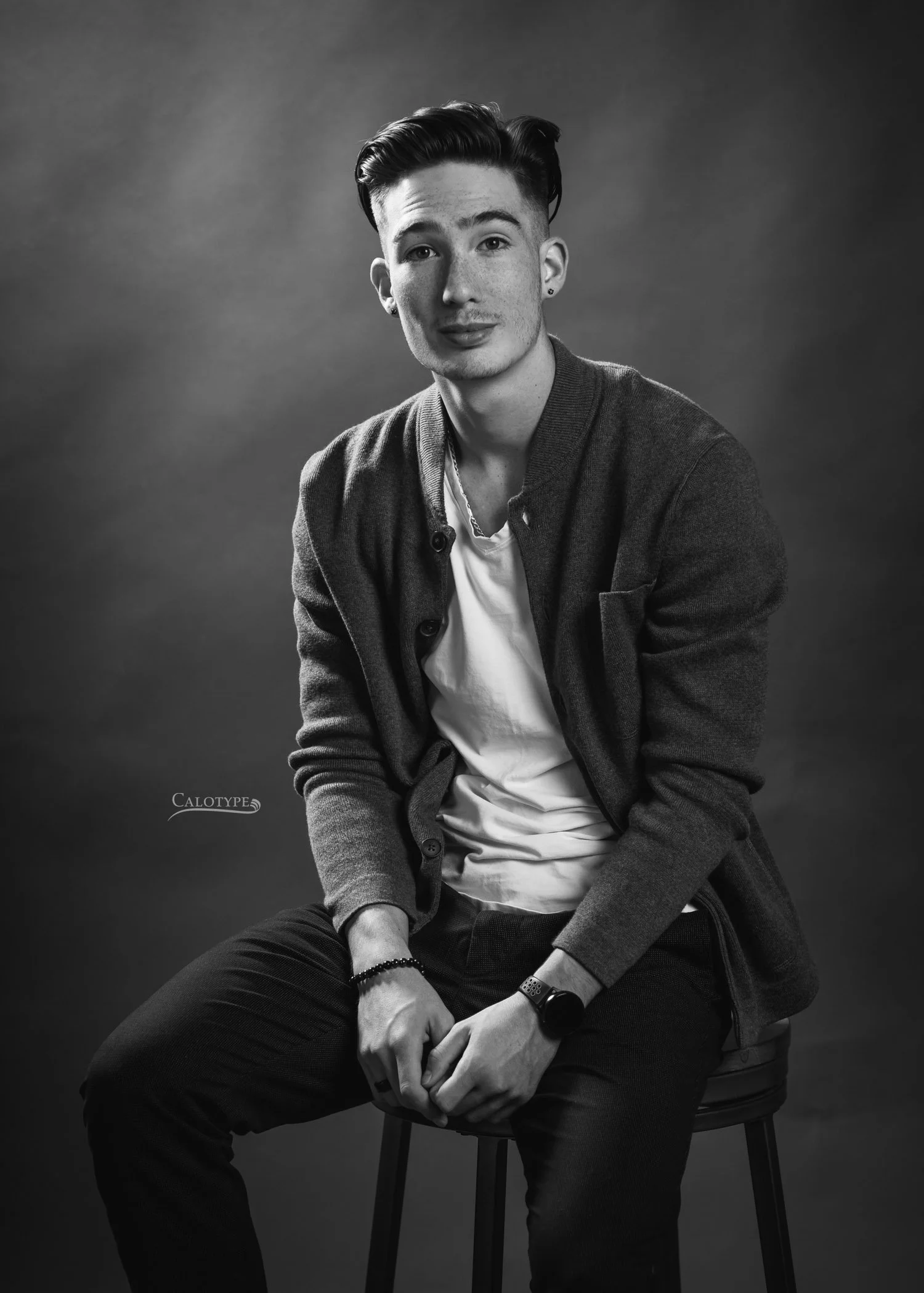class of 2022 senior photographed in black and white, sitting casually on stool in studio