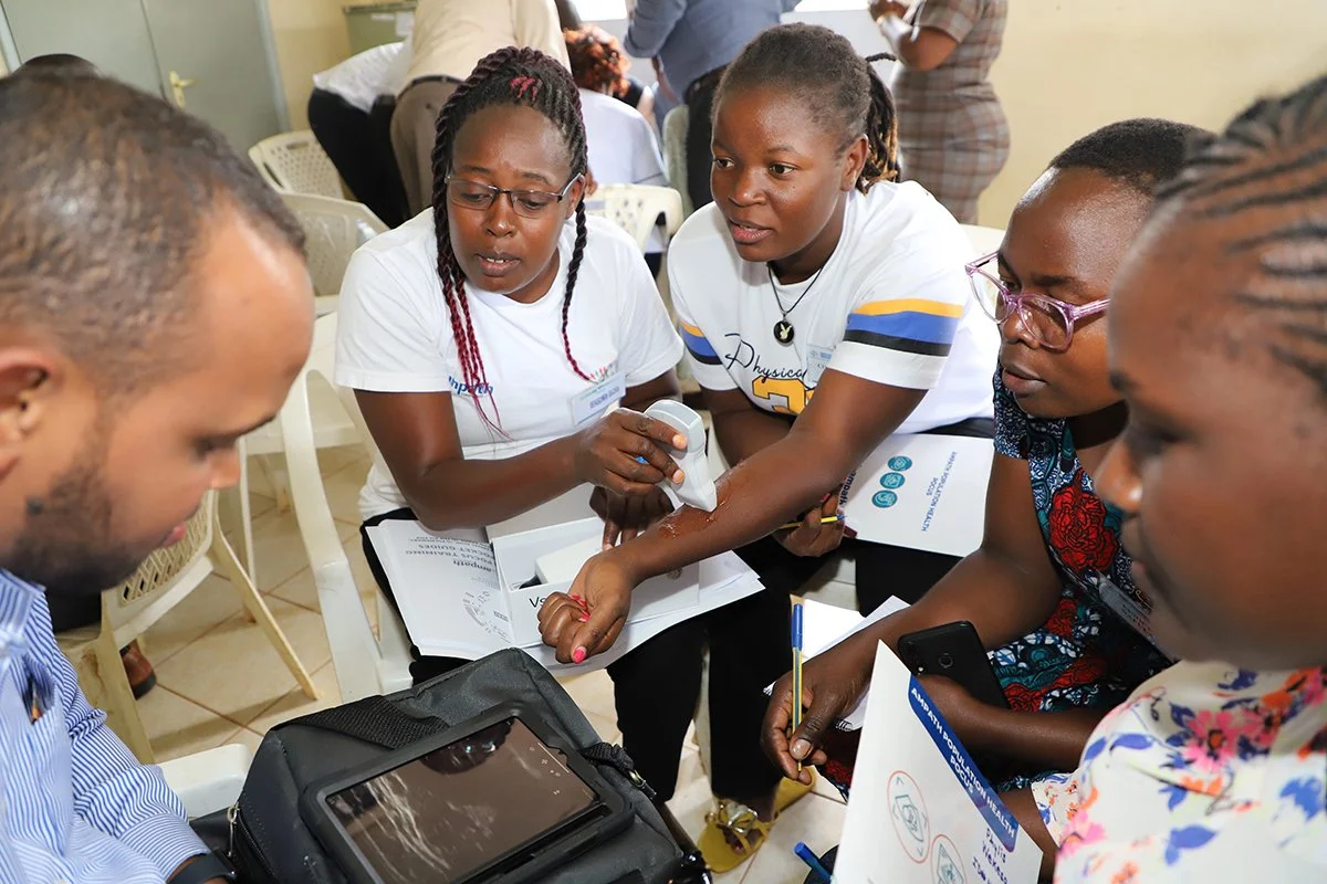 5 people sitting in a circle looking at a screen and using a POCUS device